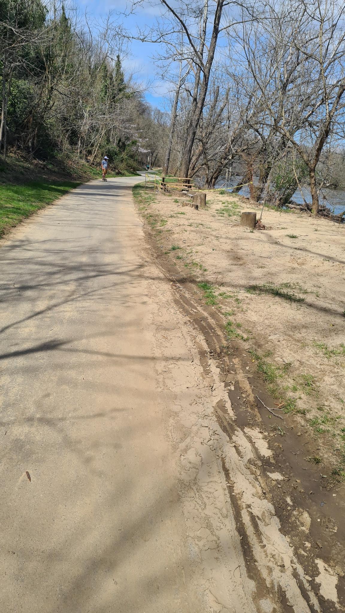 Paved path alongside a river with trees and a distant person.