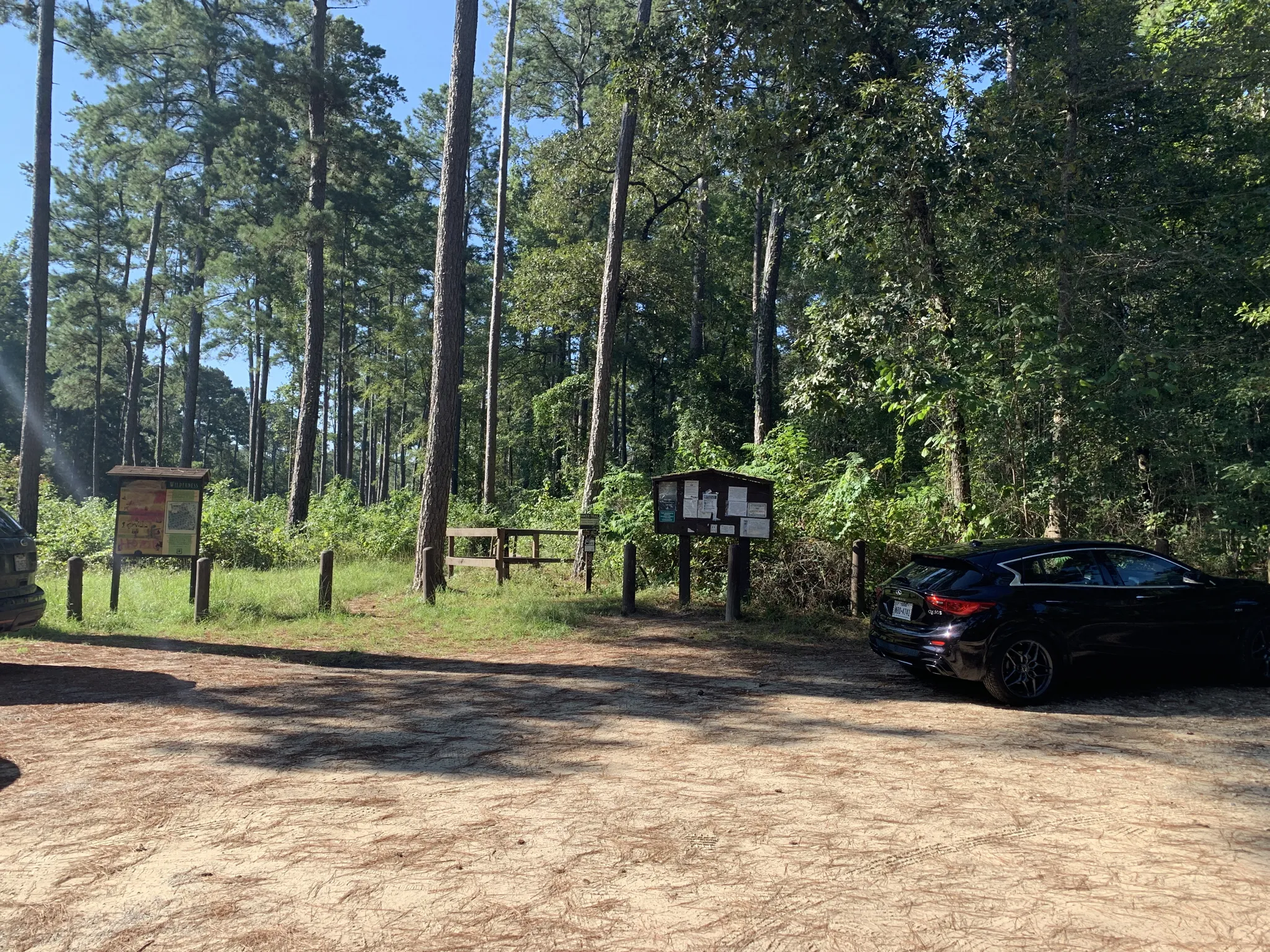 A black car parked on a dirt lot next to forest information boards. - Little Lake Creek Loop Trail