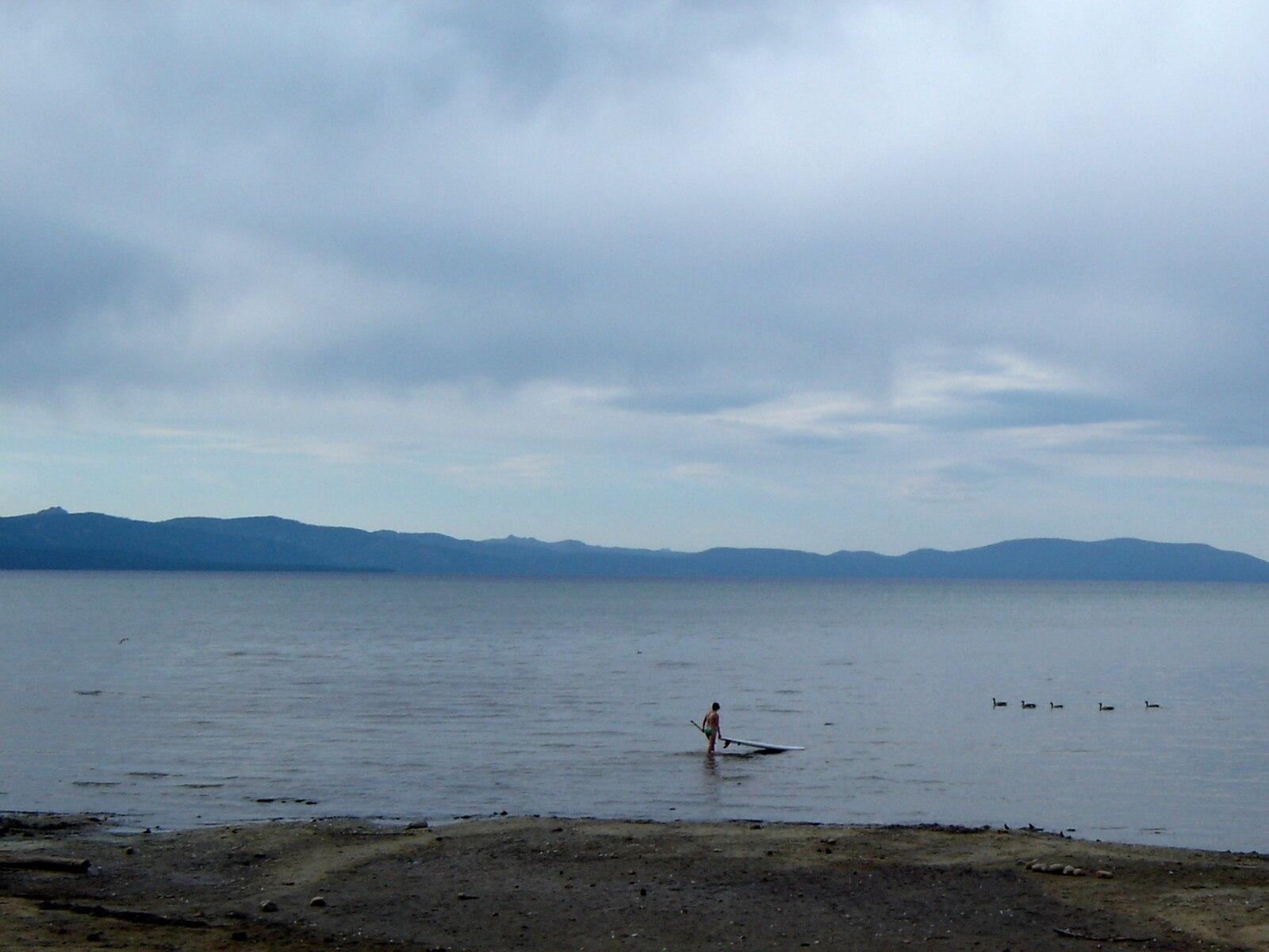 Person paddleboarding on a calm lake under an overcast sky with distant mountains.