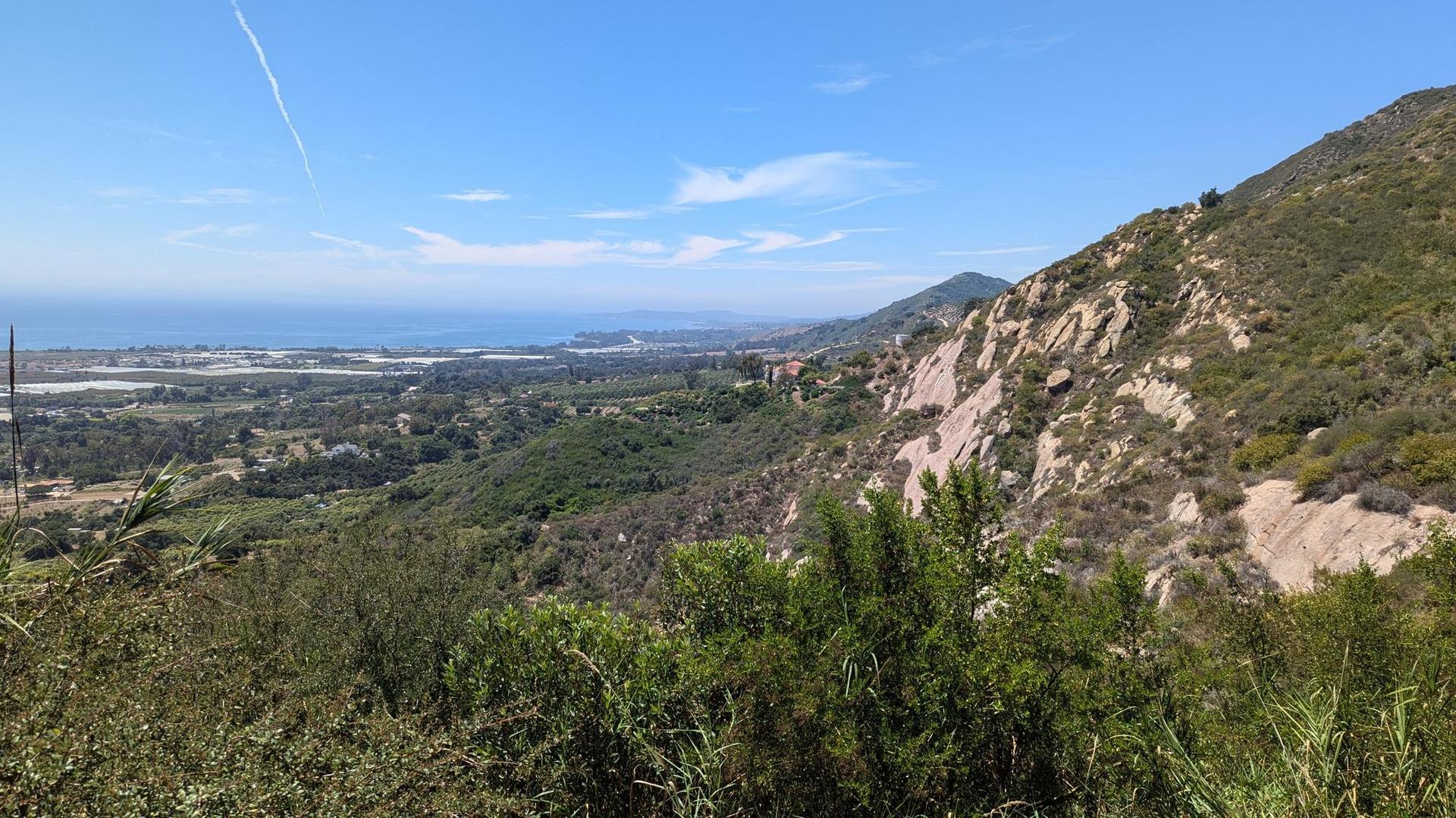 Steep rocky mountain and green hills overlook a distant coastal town and ocean.