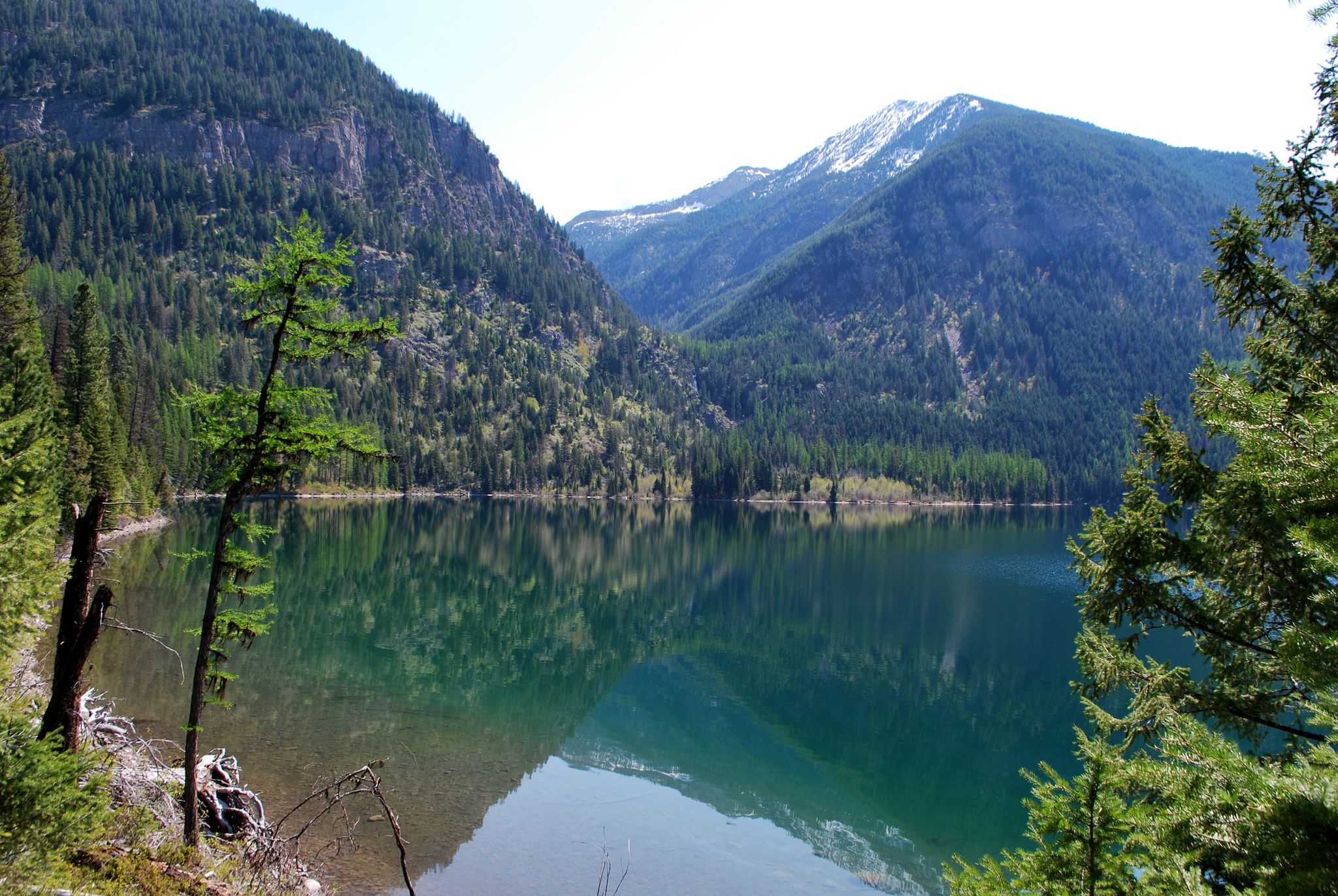 Calm lake reflecting steep, forested mountains under a bright, clear sky. - Holland Falls Trail
