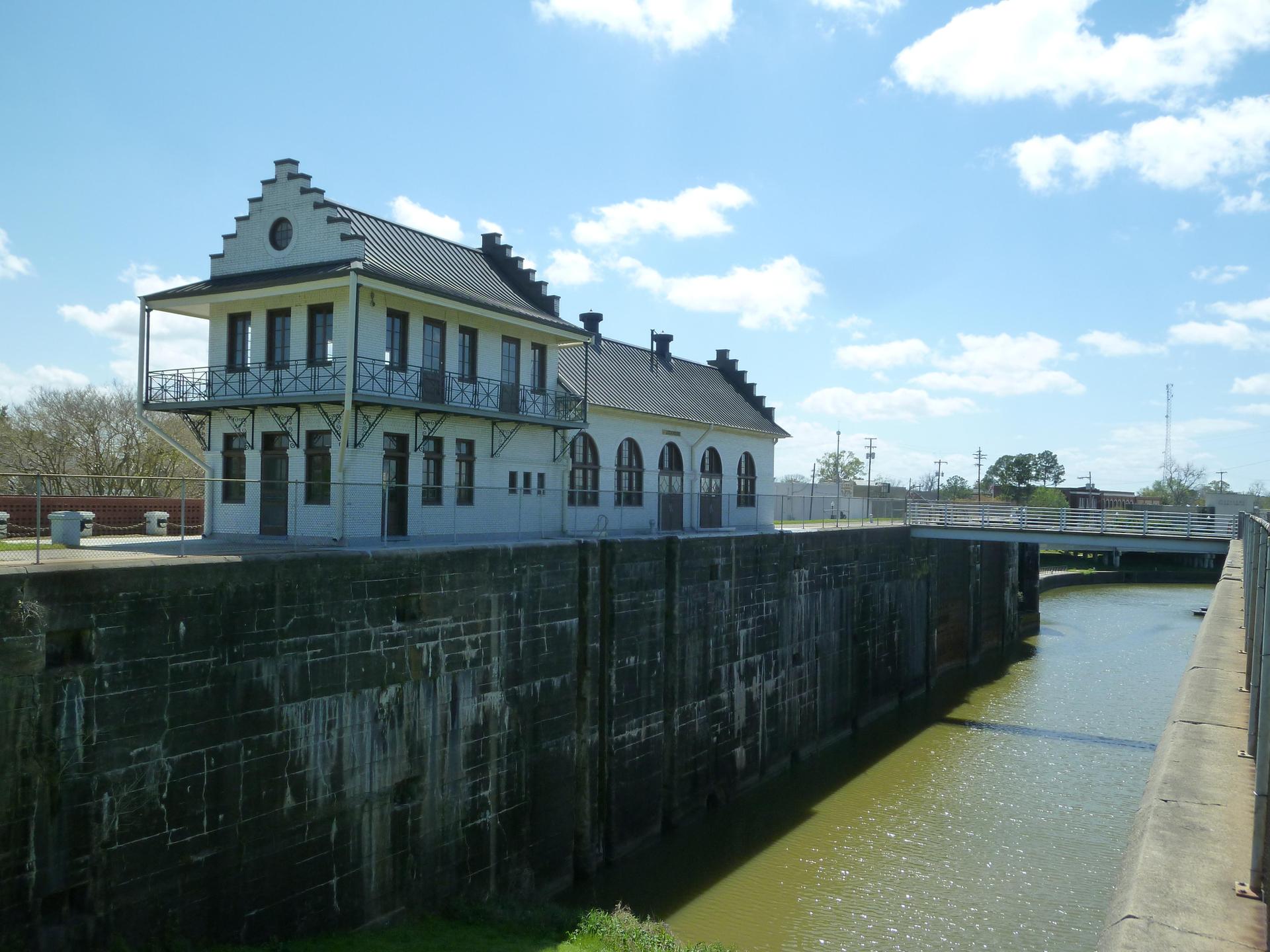White building with dark roof beside a canal lock under a sunny sky.