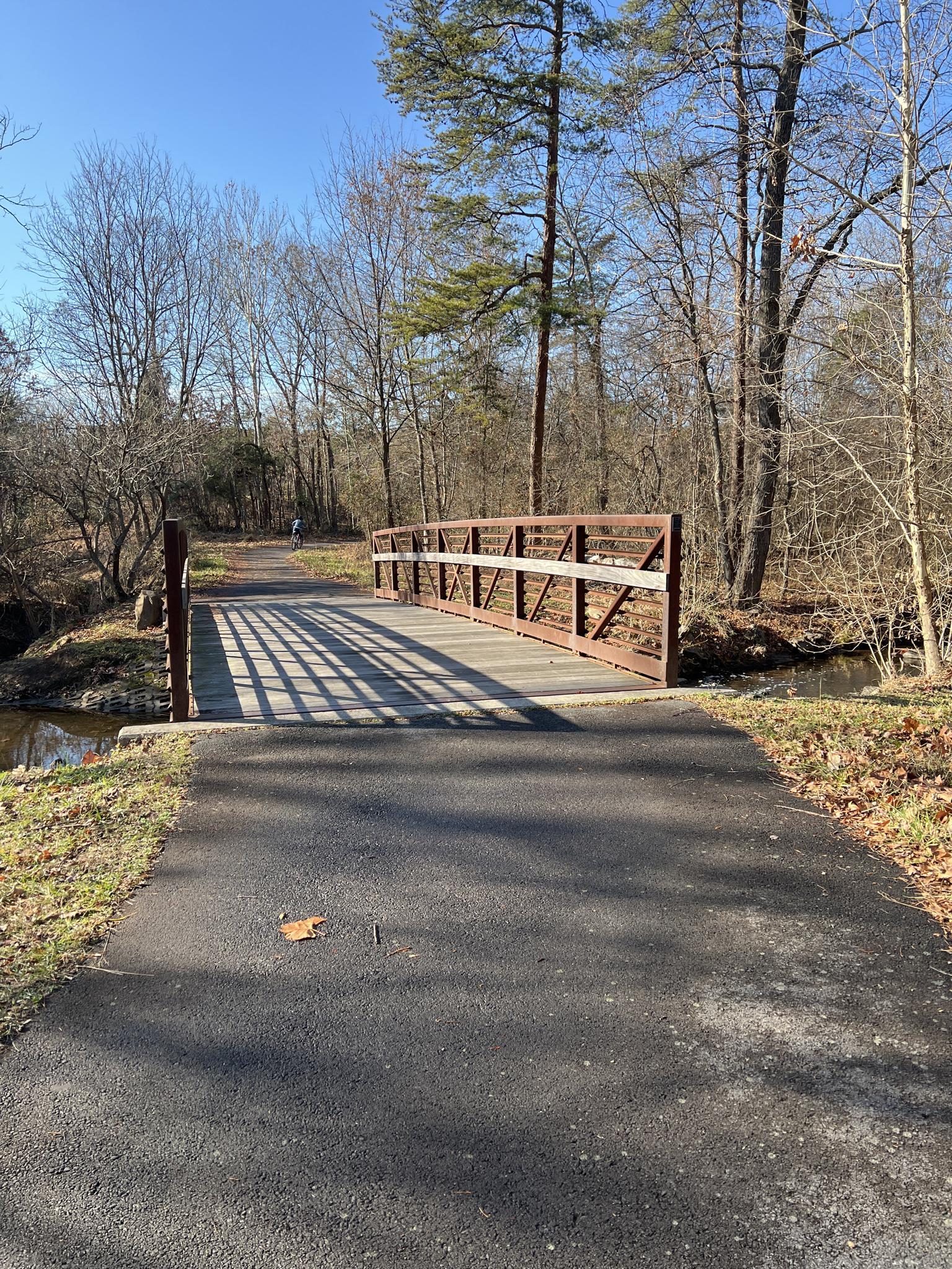 Paved path leading to a wooden and metal bridge over a stream.