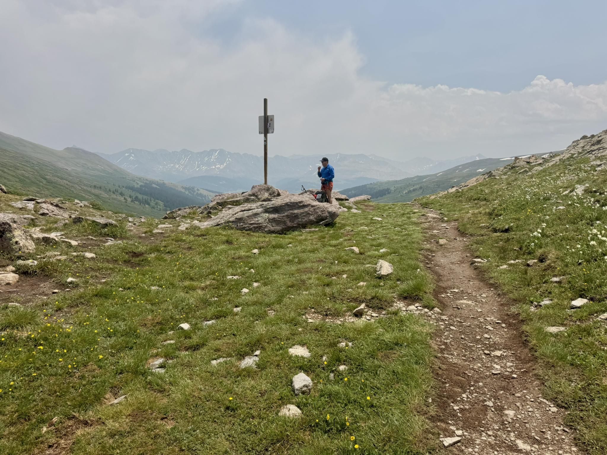 Person stands by a signpost on a rocky mountain path under cloudy skies. - Colorado Trail: Copper Mountain to Searle Pass
