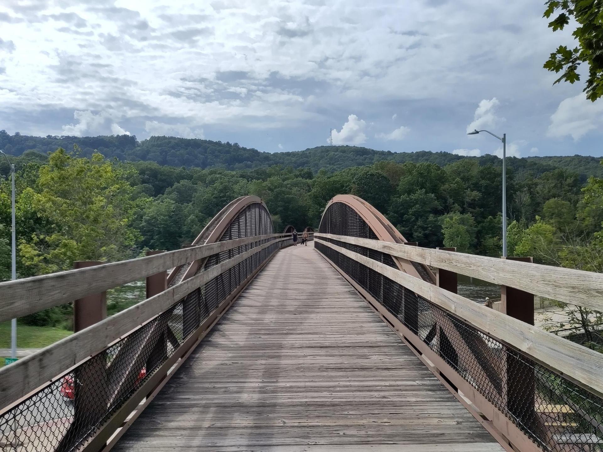 A long wooden pedestrian bridge with arched supports extends over a valley.