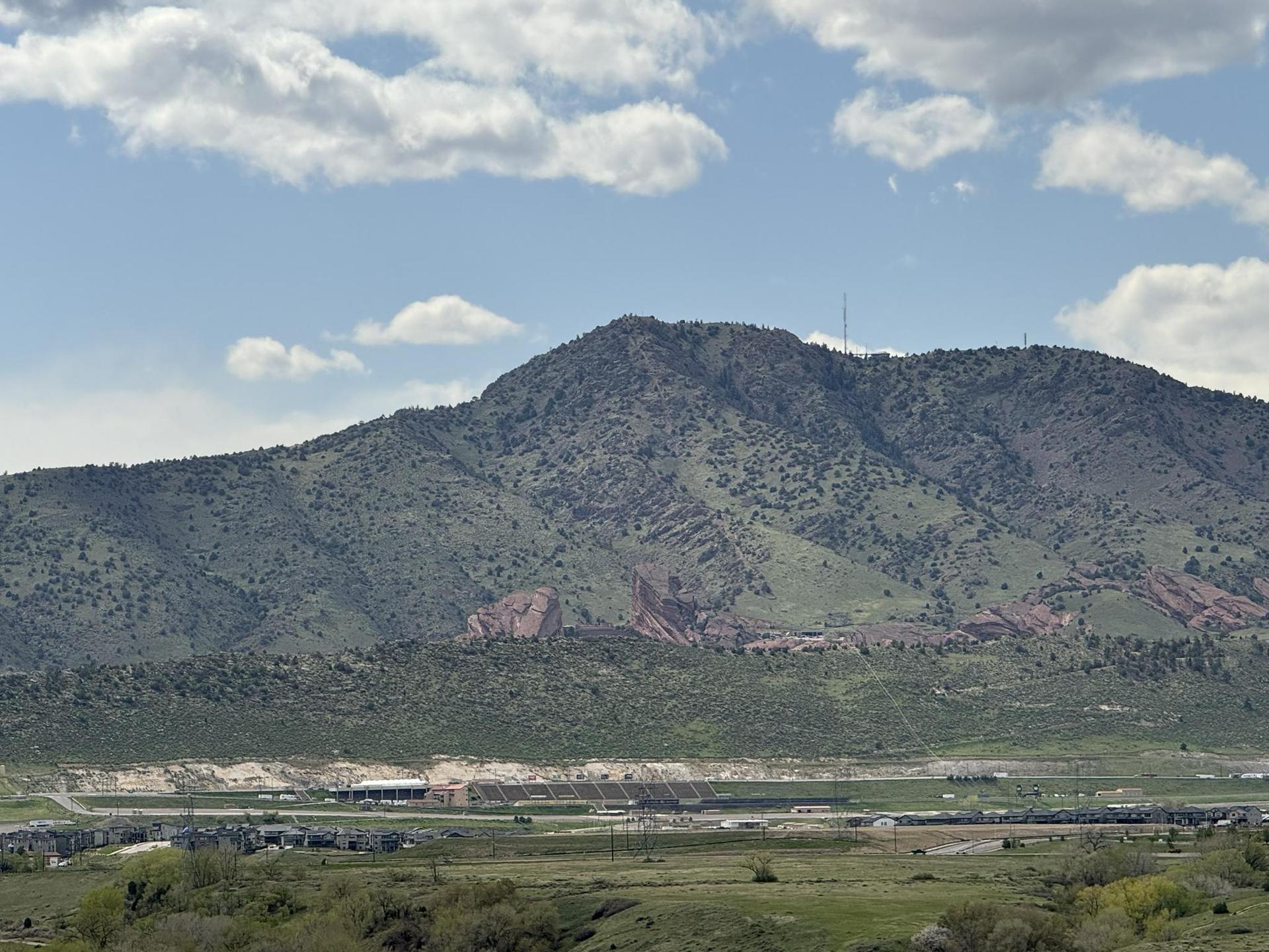 Green mountain with rocky outcrops overlooking a valley on a bright day.