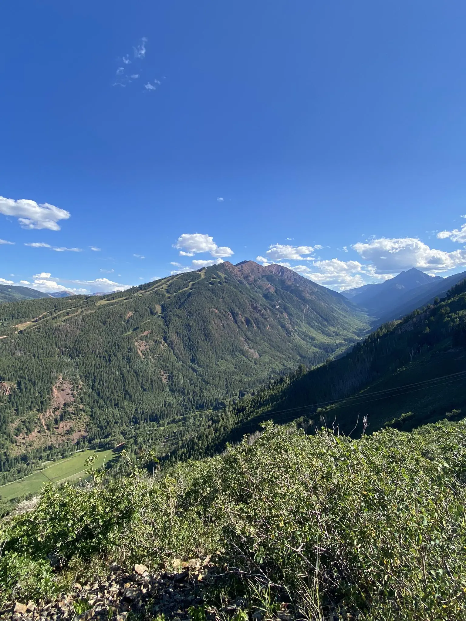 Expansive view of green mountains and a valley under a bright blue sky.