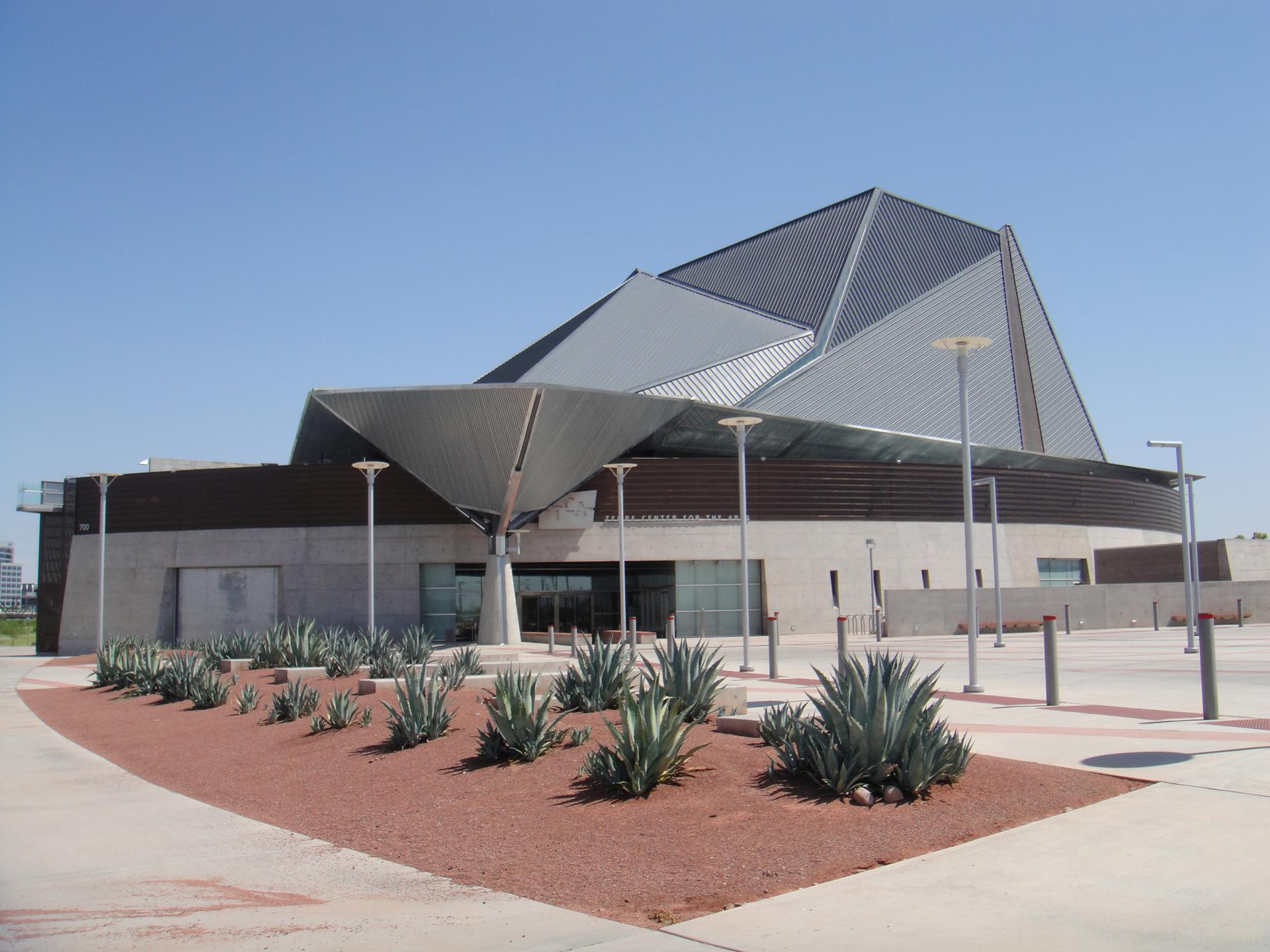Striking modern building with angular roof and agave plants under clear sky.