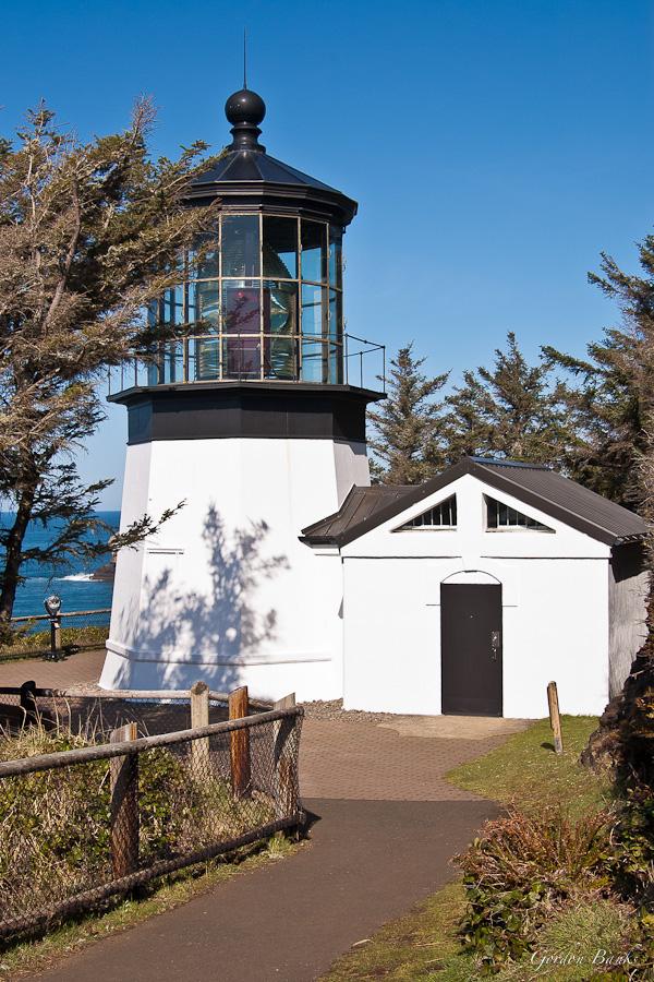 White lighthouse with black top next to a small building on a sunny day.