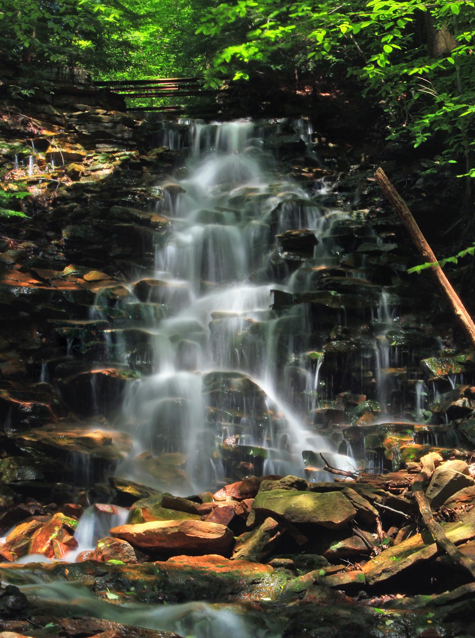 A beautiful multi-tiered waterfall cascades over dark rocks in a lush forest.