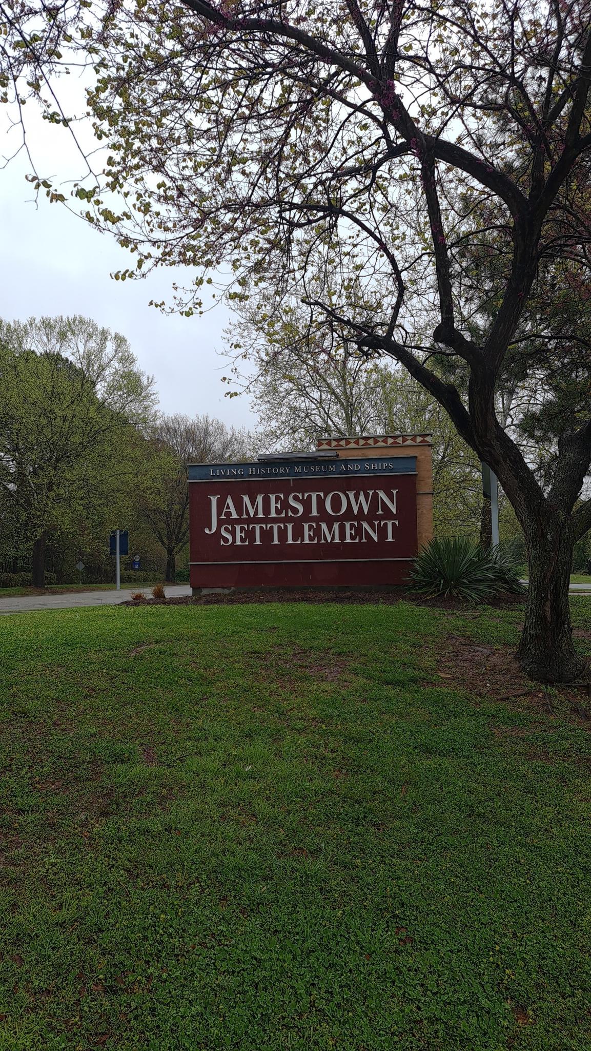 A large brown sign under bare trees on a grassy hill, overcast day.