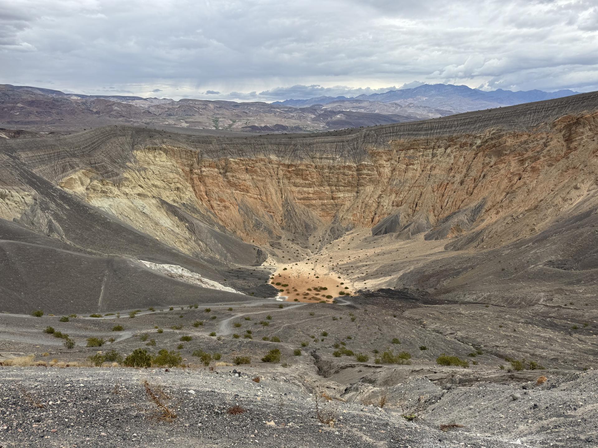 Wide view of a large volcanic crater with colorful walls under an overcast sky.