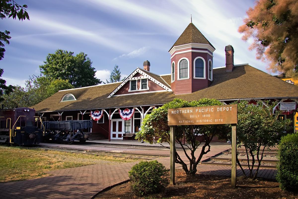 A historic red and white building with a tower, a train, and a sign.
