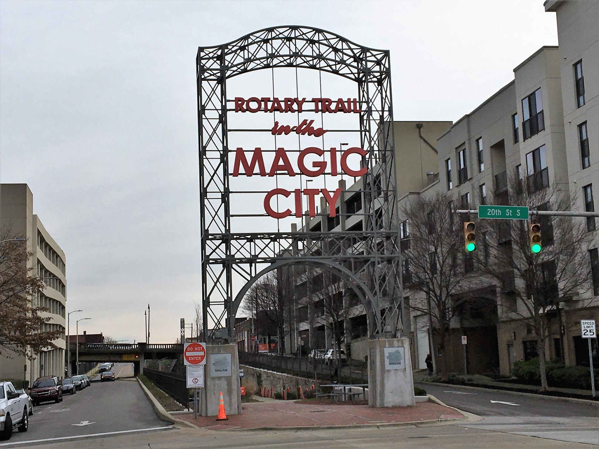 Large metal archway sign with red text over a street in an urban setting.