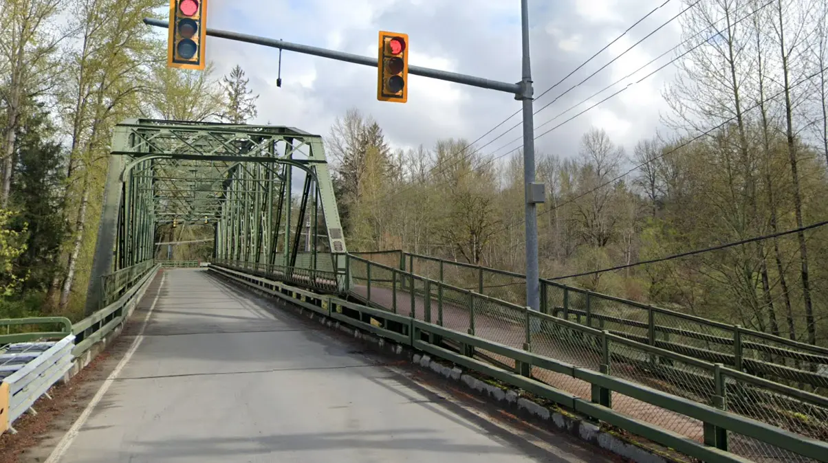 Green metal truss bridge with traffic lights under an overcast sky.