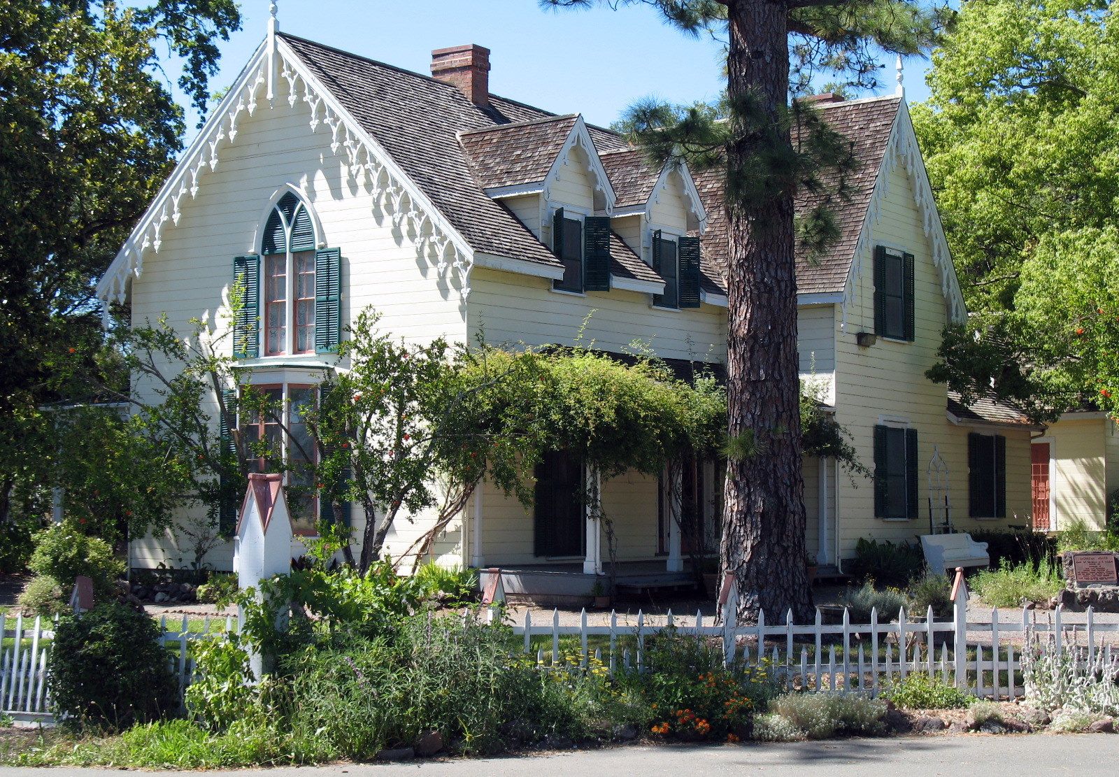 An ornate yellow Victorian house with a white fence on a sunny day. - Bike Path