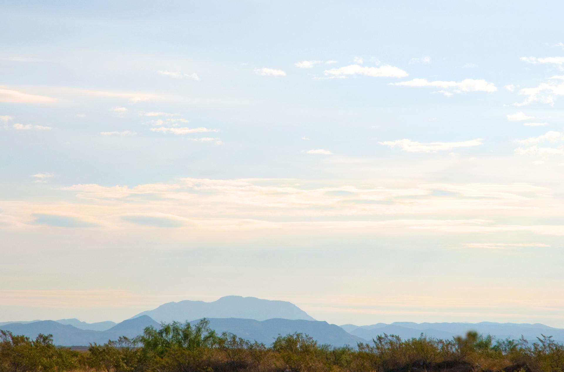 Hazy distant mountains over a desert landscape with sparse vegetation under a soft sky.
