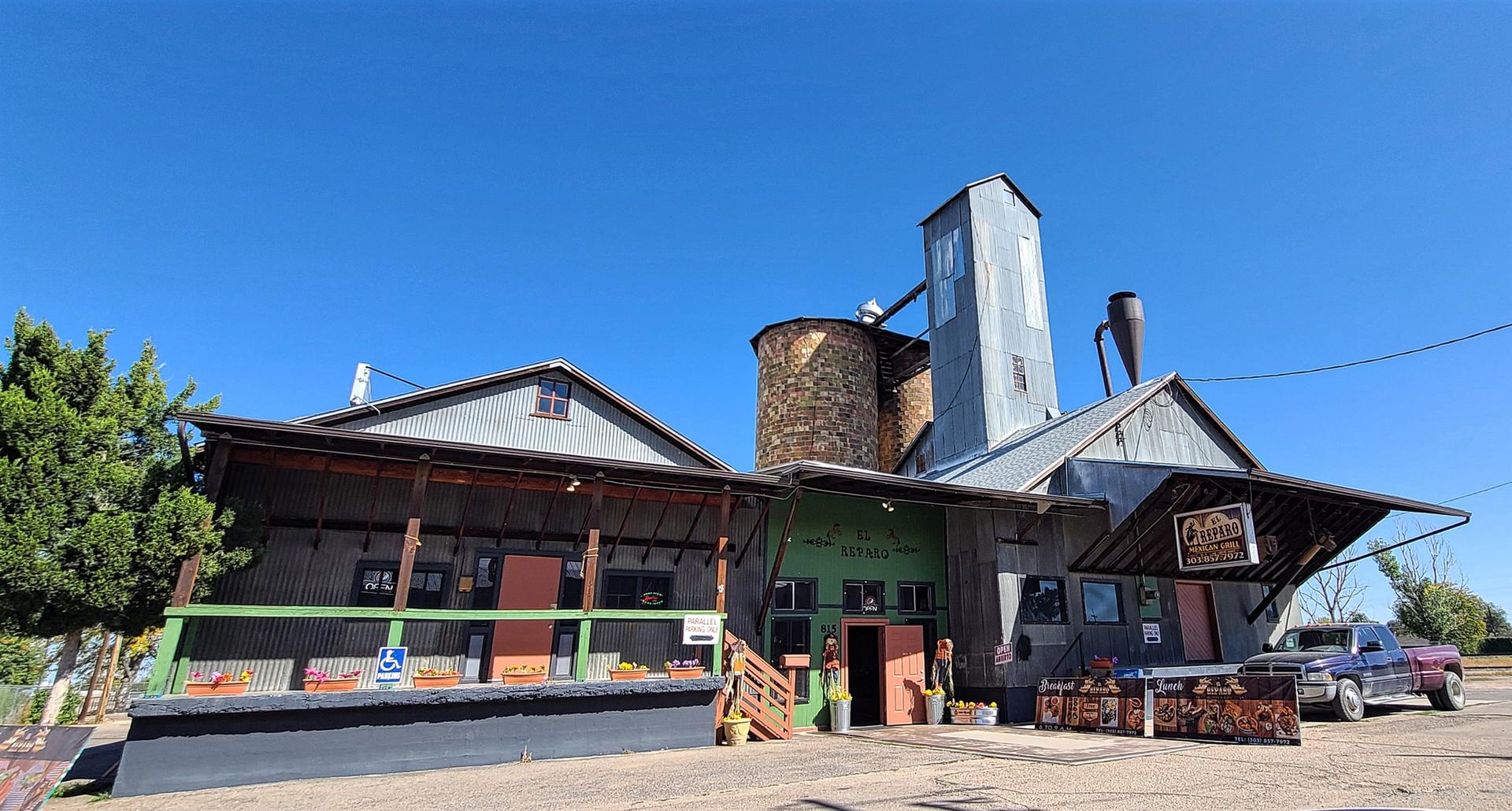 Industrial-style building with silo and parked truck under a clear blue sky.