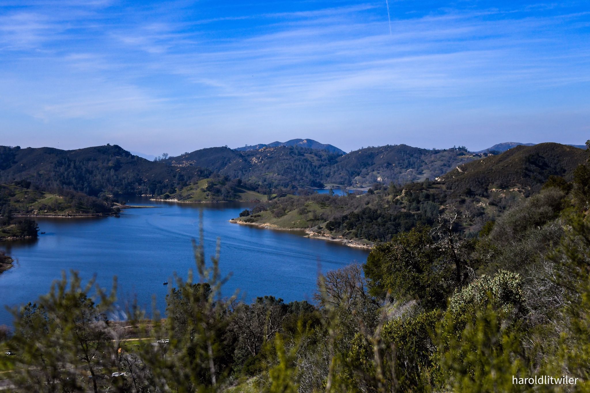 A large blue lake surrounded by green, tree-covered hills under a clear sky. - Grey Pine and Rocky Trail Loop