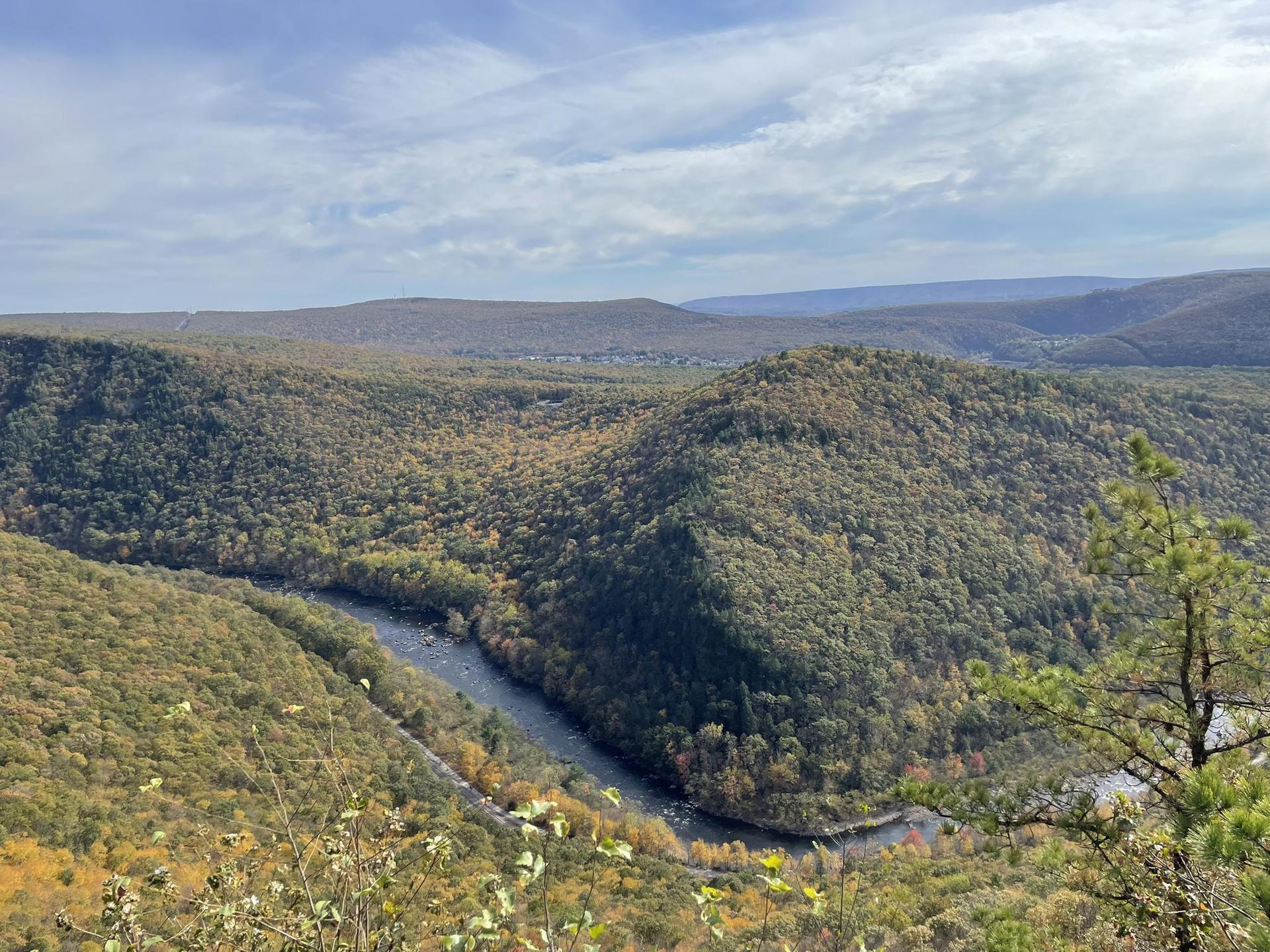 A wide river winds through a vast, forested mountain valley under a cloudy sky.
