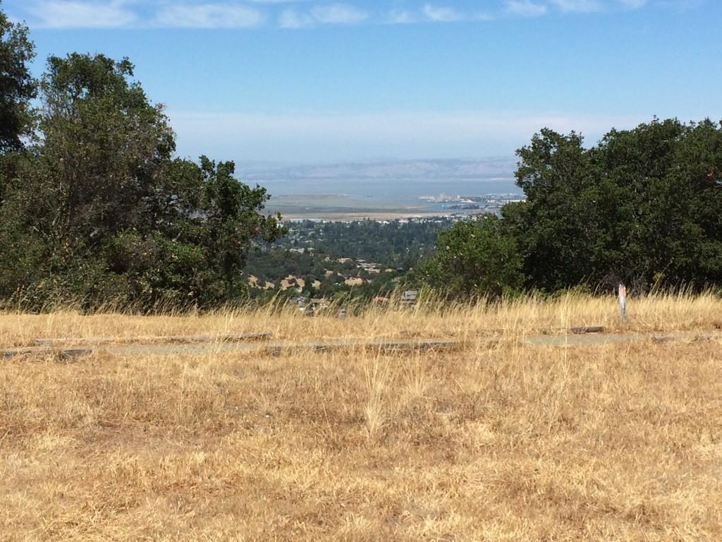 Dry grassy hill overlooking a valley with distant water under a clear sky.