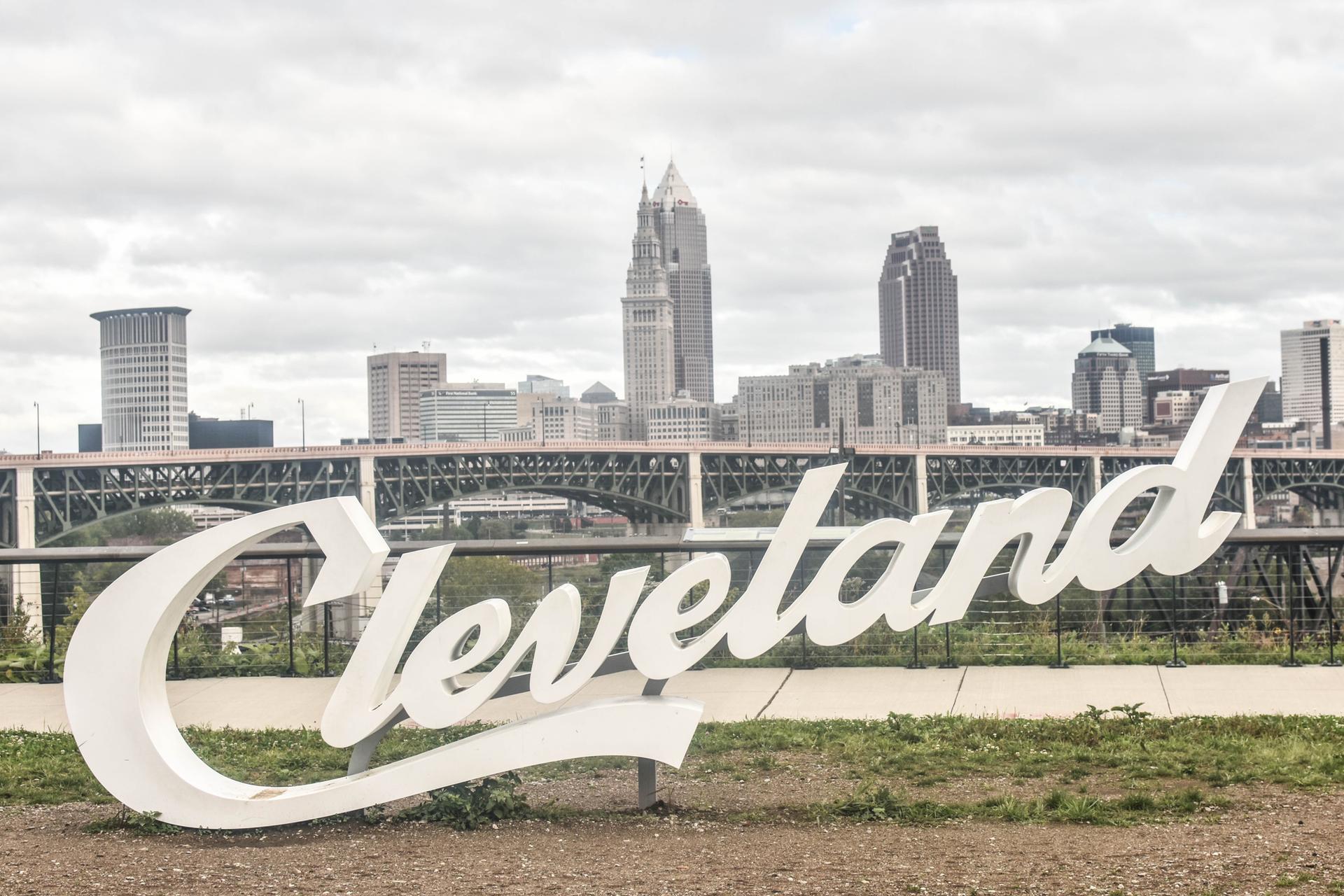 Large white sign in foreground with city skyline and bridge under cloudy sky.