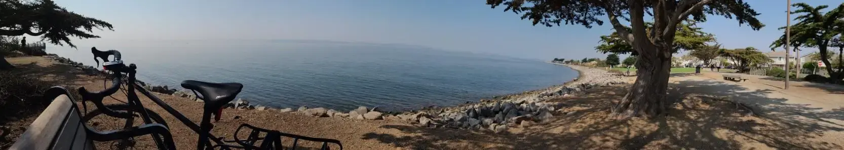 Bicycle and bench near a calm body of water under a sunny sky.