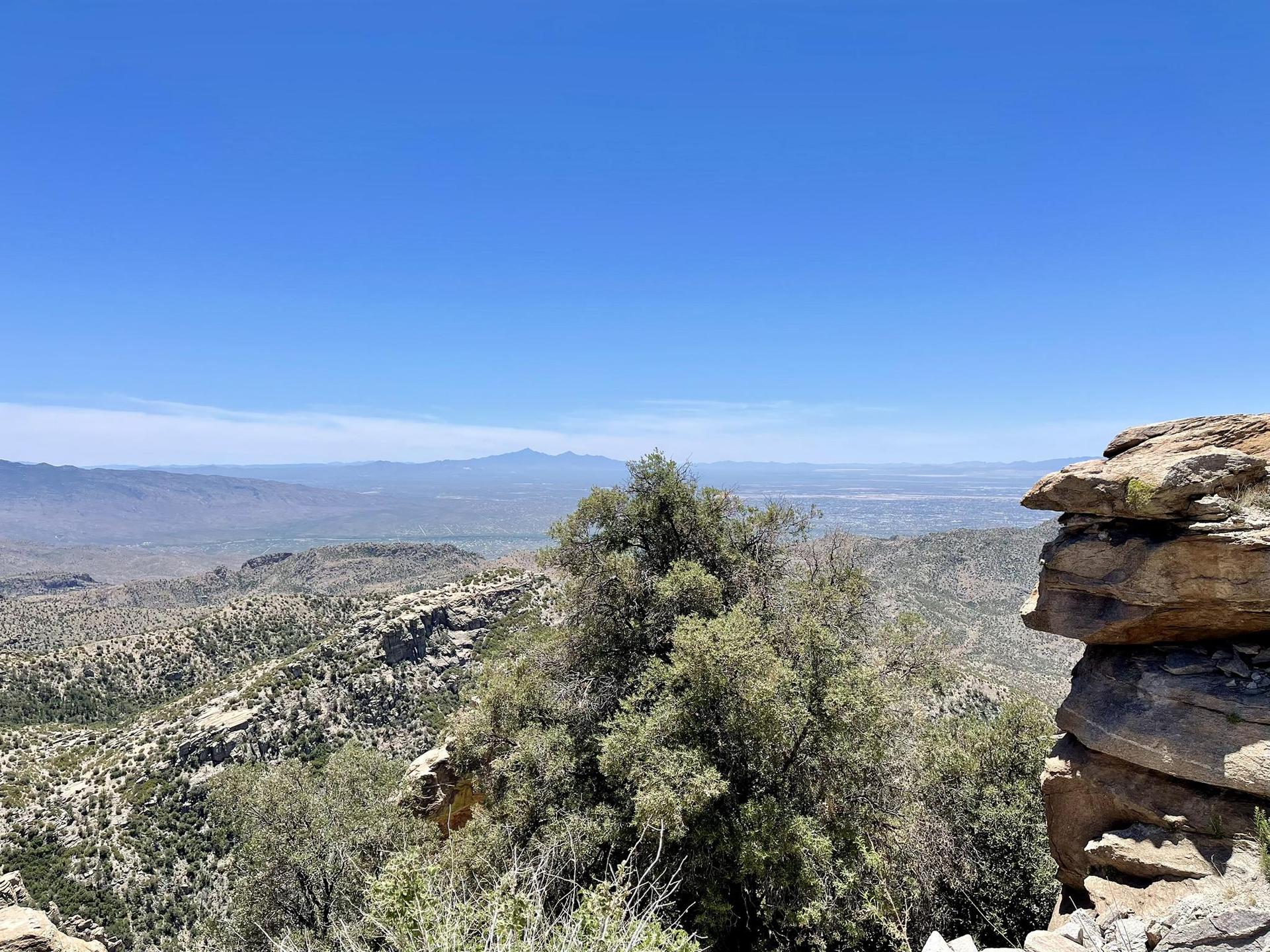 Vast mountain landscape with a rocky outcrop and distant valleys under clear sky.