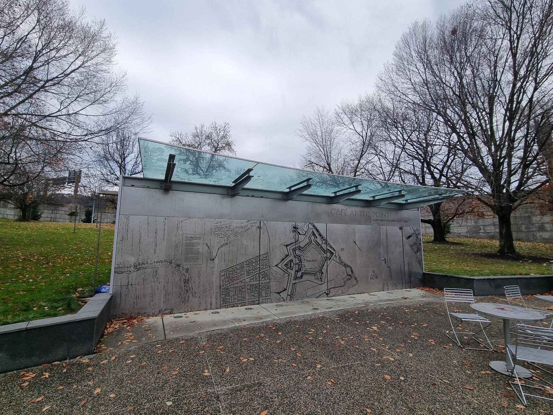 Modern concrete structure with glass canopy in a park on an overcast day.