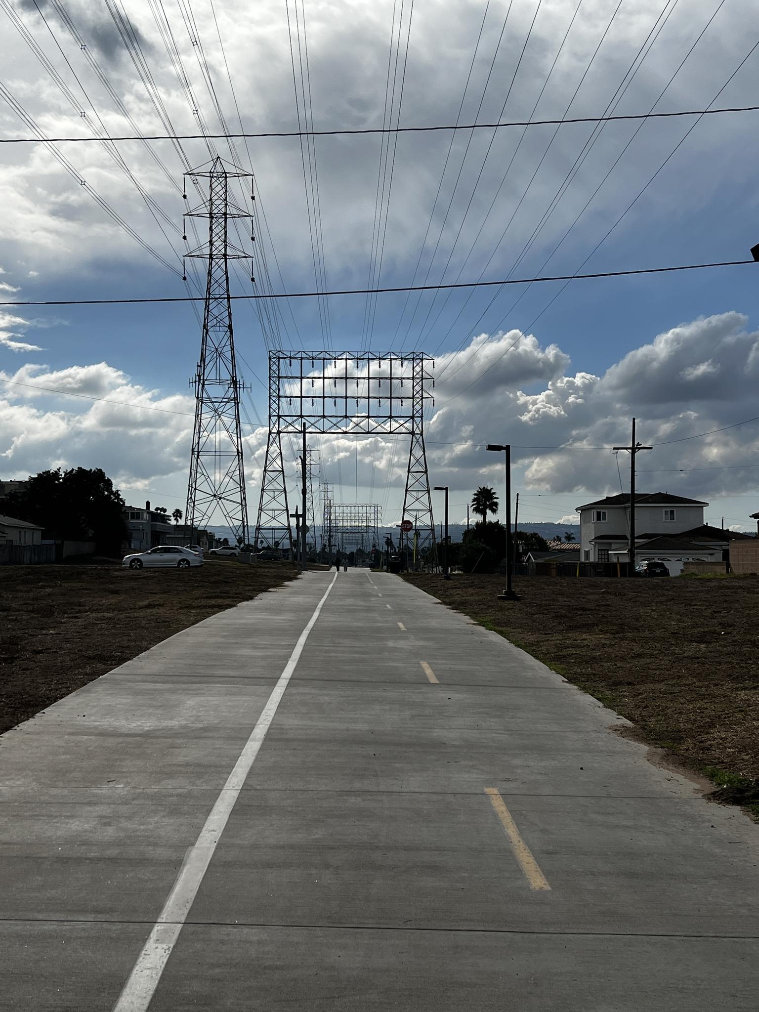 A paved path leading towards large power lines and transmission towers.