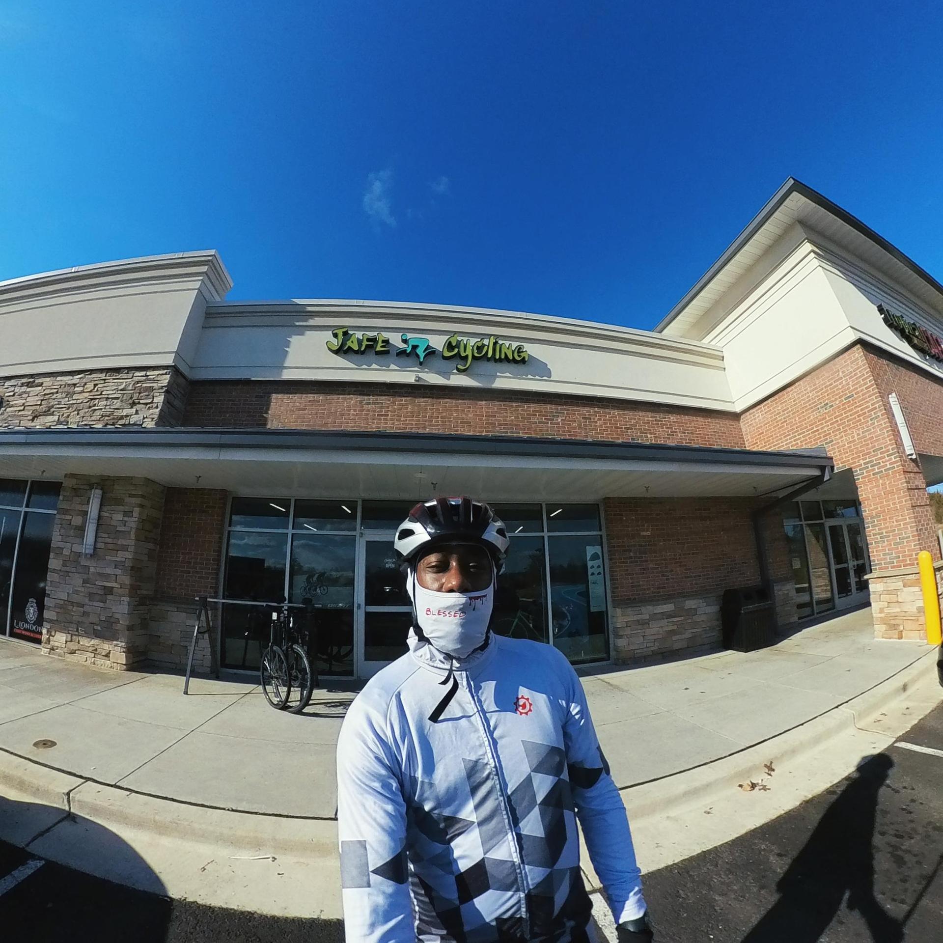 Cyclist in helmet and mask stands in front of a building on a sunny day.