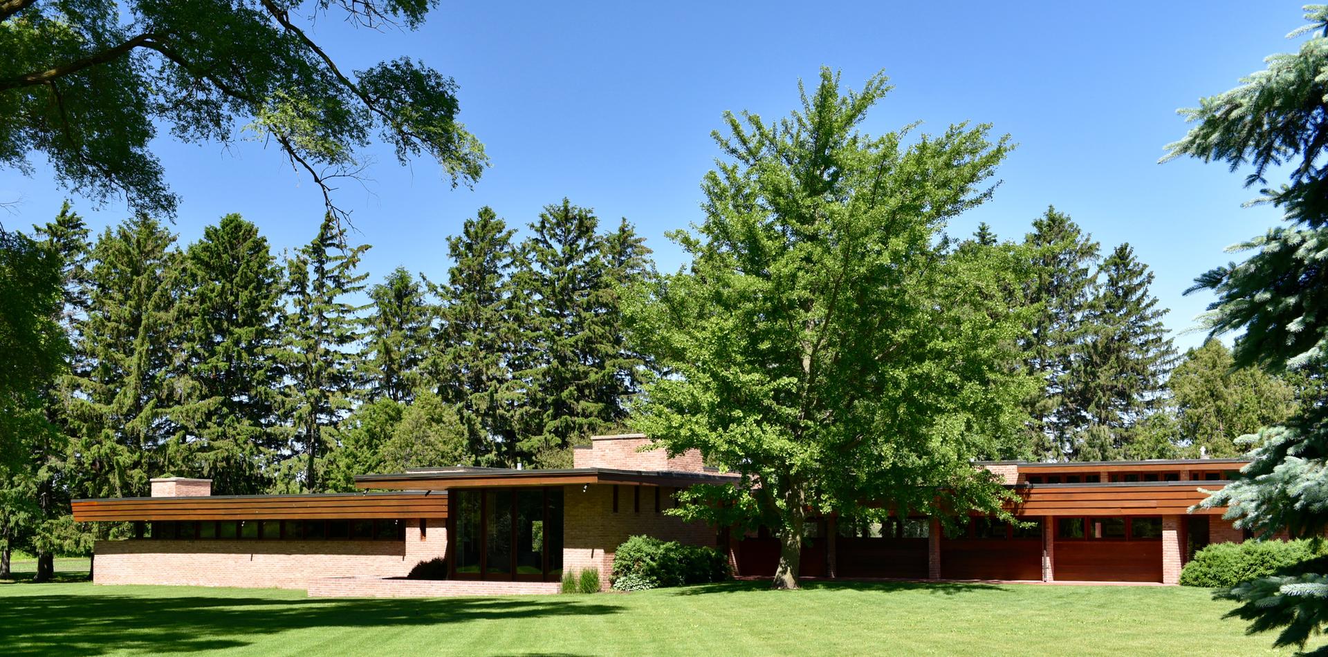 A low-profile building on a green lawn, surrounded by dense trees under a clear sky.