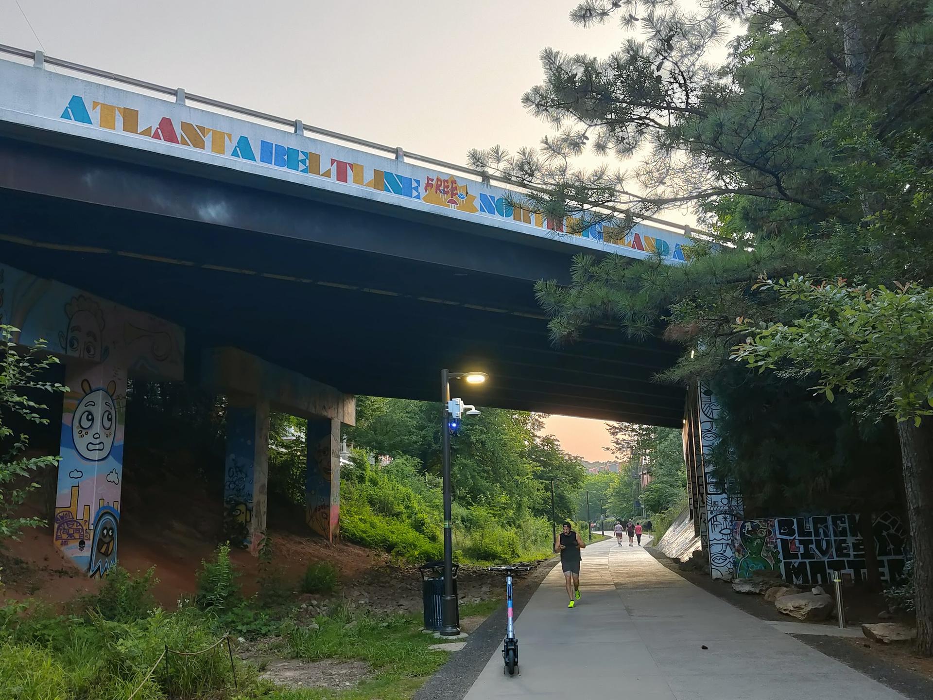 Paved path under a bridge with colorful murals, a jogger, and an electric scooter.