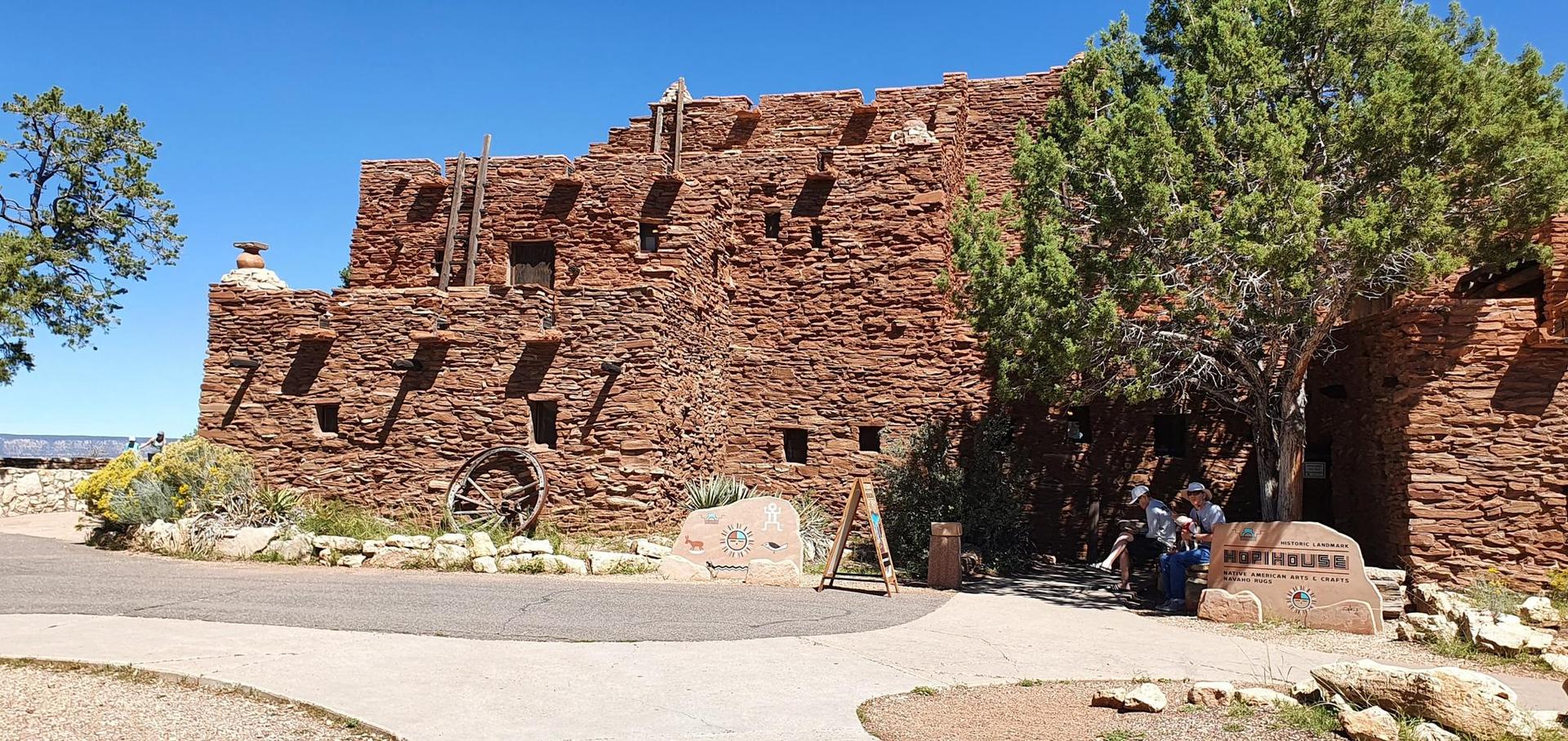 Stone building with small windows and people sitting under a tree.