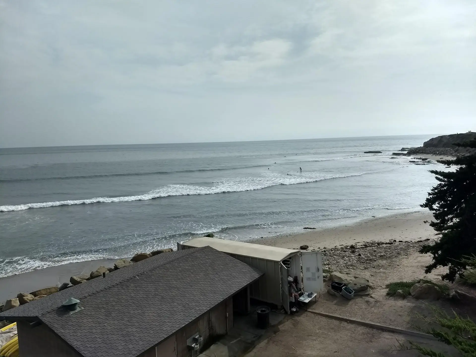 Aerial view of a beach with surfers in waves and two buildings.