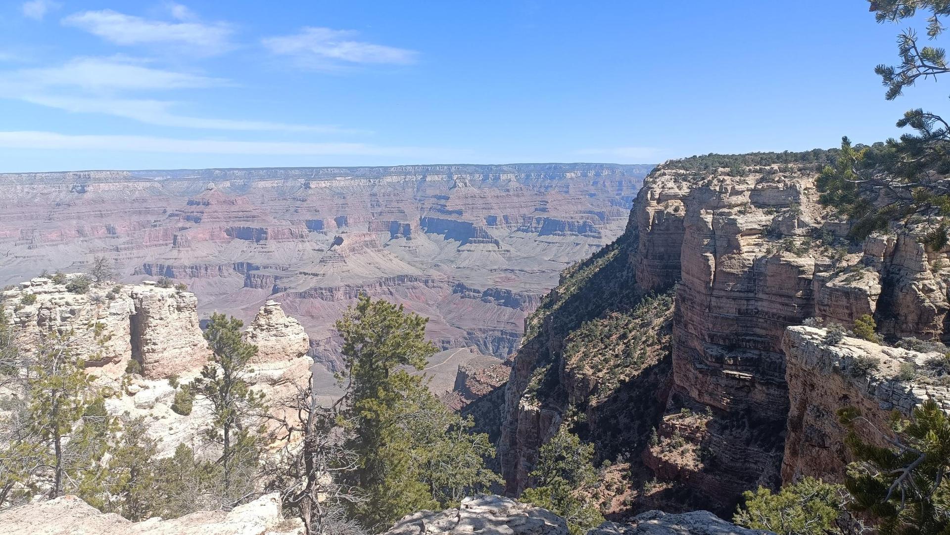 Expansive canyon view with distant layered rock formations under a clear blue sky.