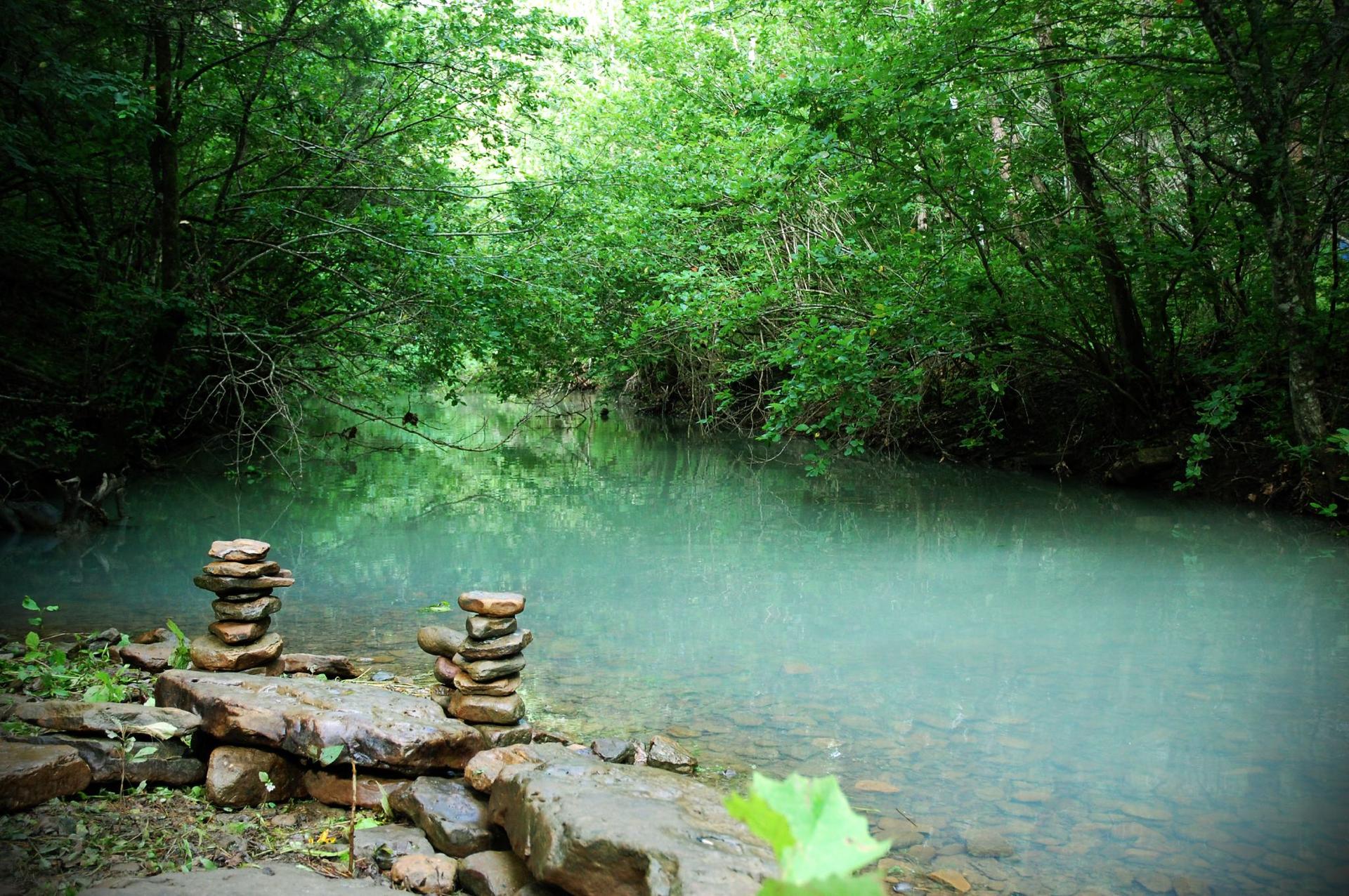 Two rock cairns beside a clear turquoise stream in a lush green forest.