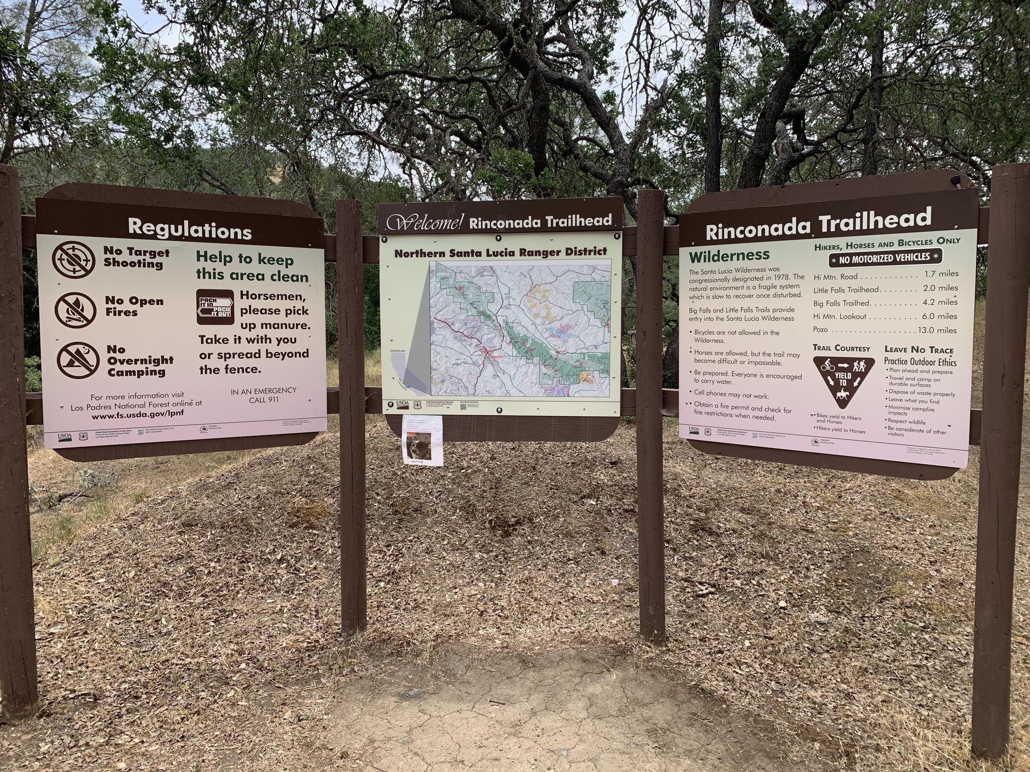 Three trailhead signs with maps and regulations on a dirt path under an overcast sky. - Rinconada Trail and Hi Mountain Lookout Road Loop