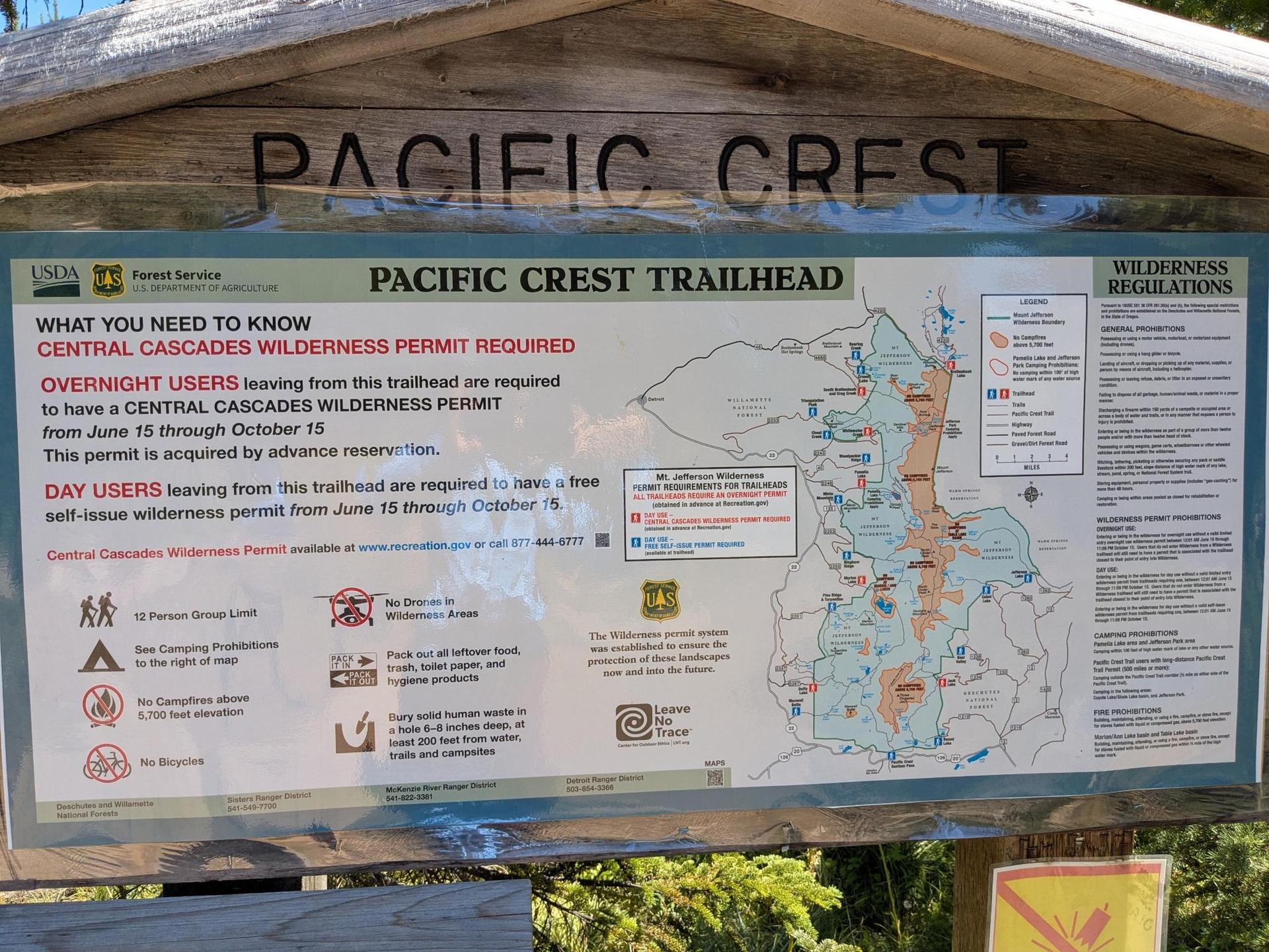 A large informational board under a wooden shelter, surrounded by trees.