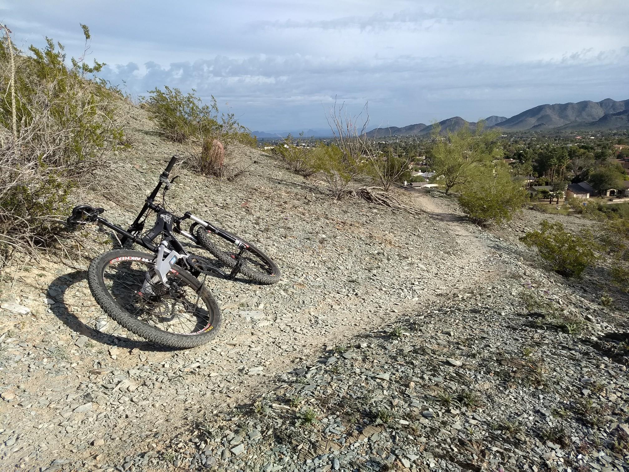 Mountain bike resting on a rocky desert trail under a bright sky.
