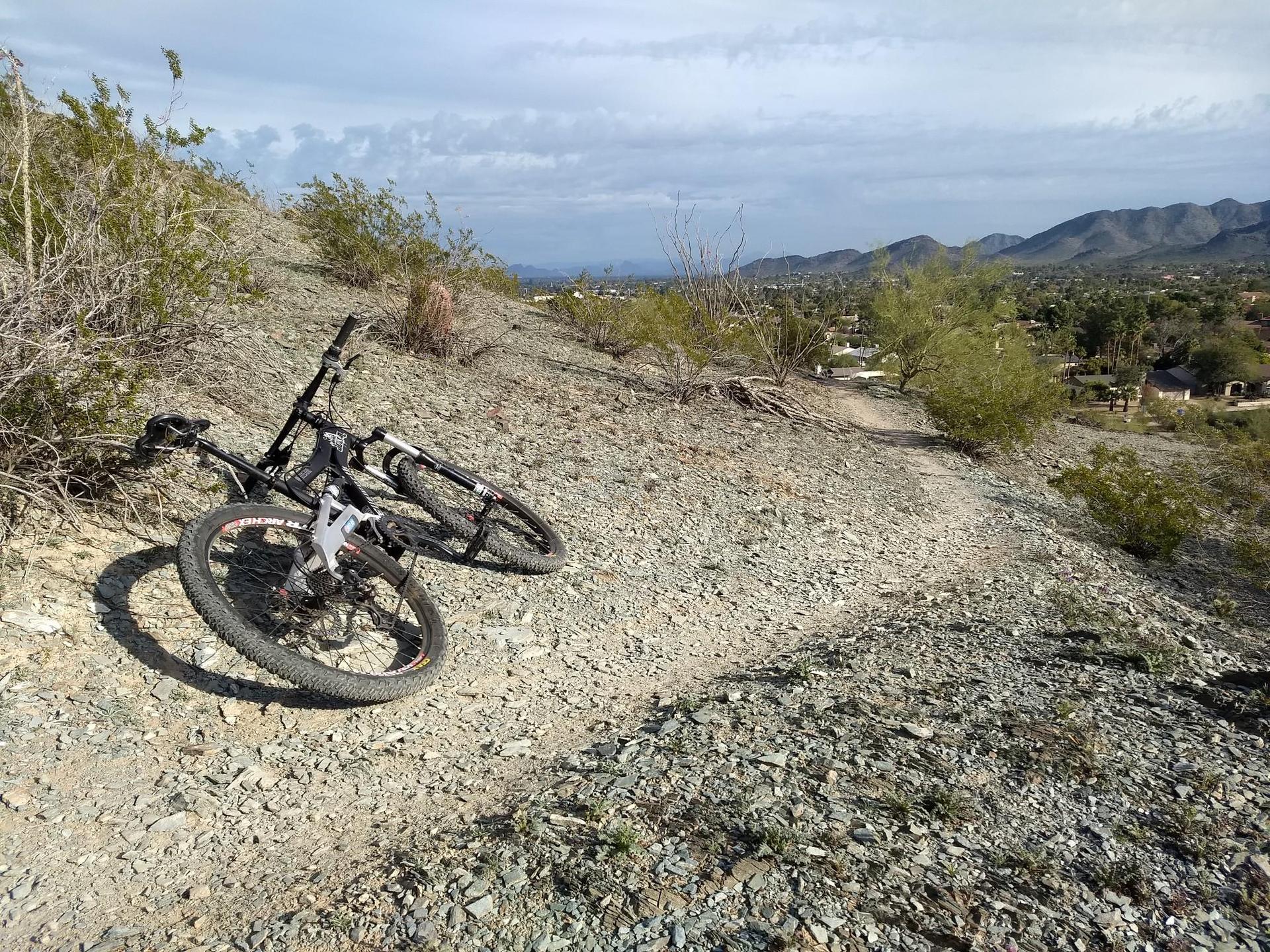 Mountain bike resting on a rocky desert trail under a bright sky.