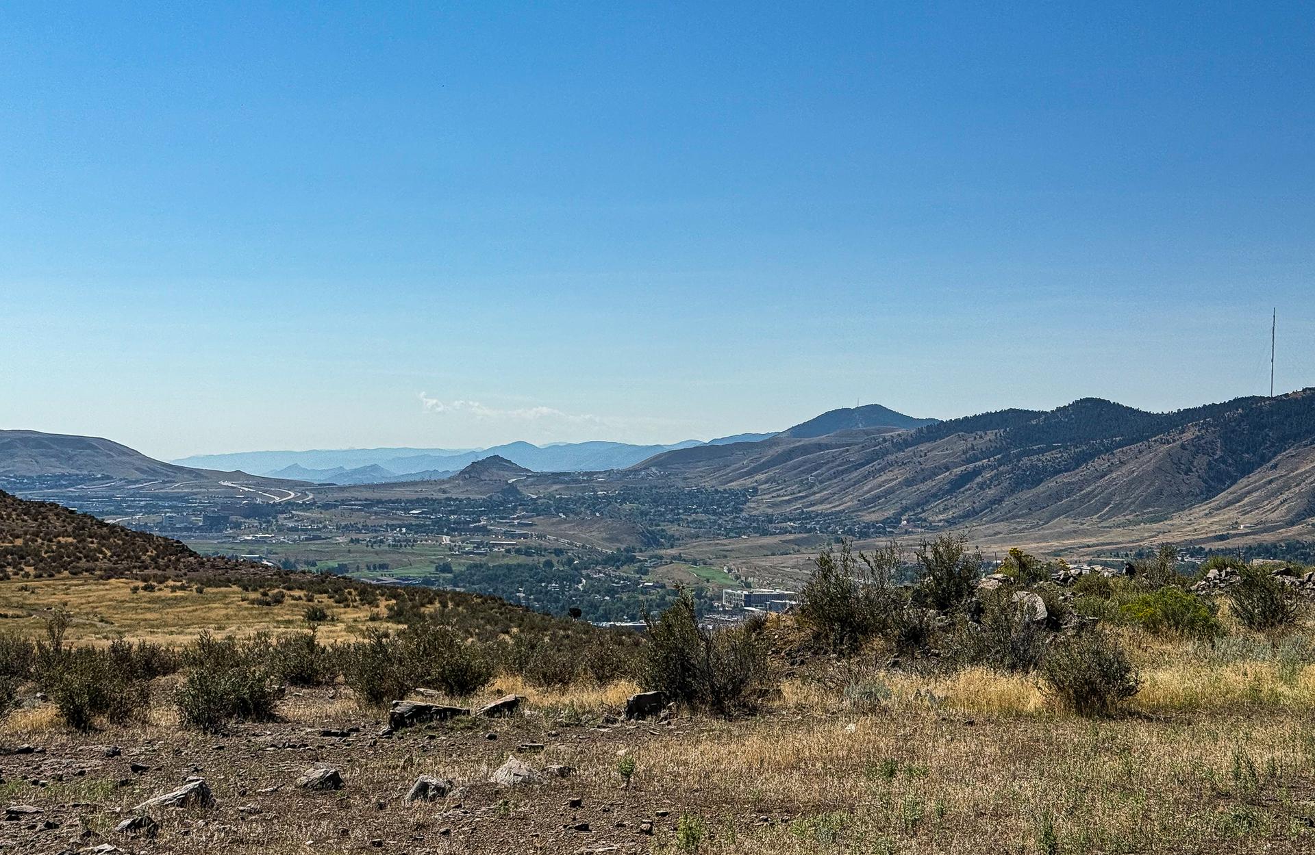 Vast mountain valley with dry hills and distant town under clear blue sky.