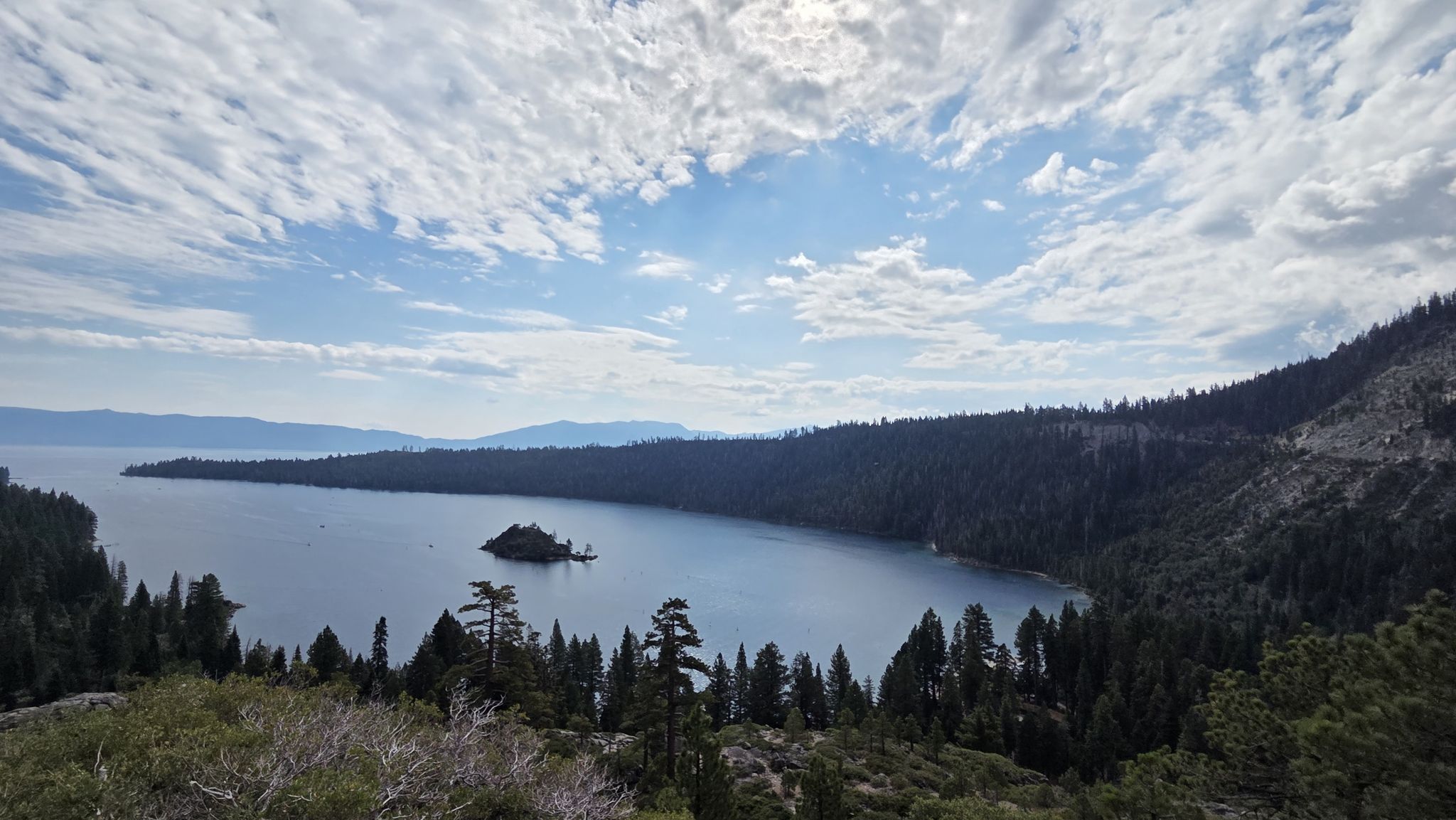 Panoramic view of a lake with an island, surrounded by forested mountains. - Eagle Falls Trail