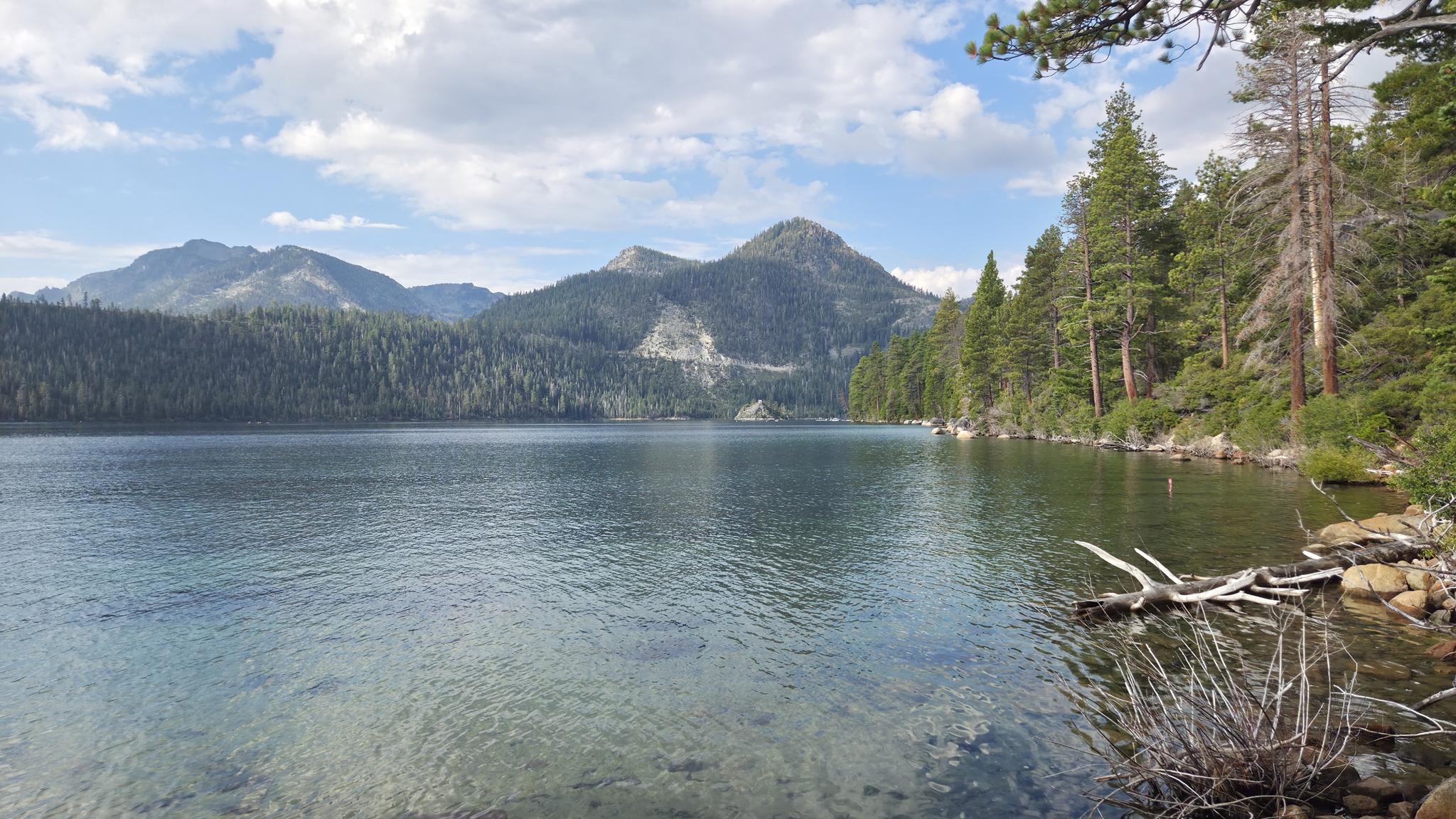 Clear lake with forested mountains under a partly cloudy sky.