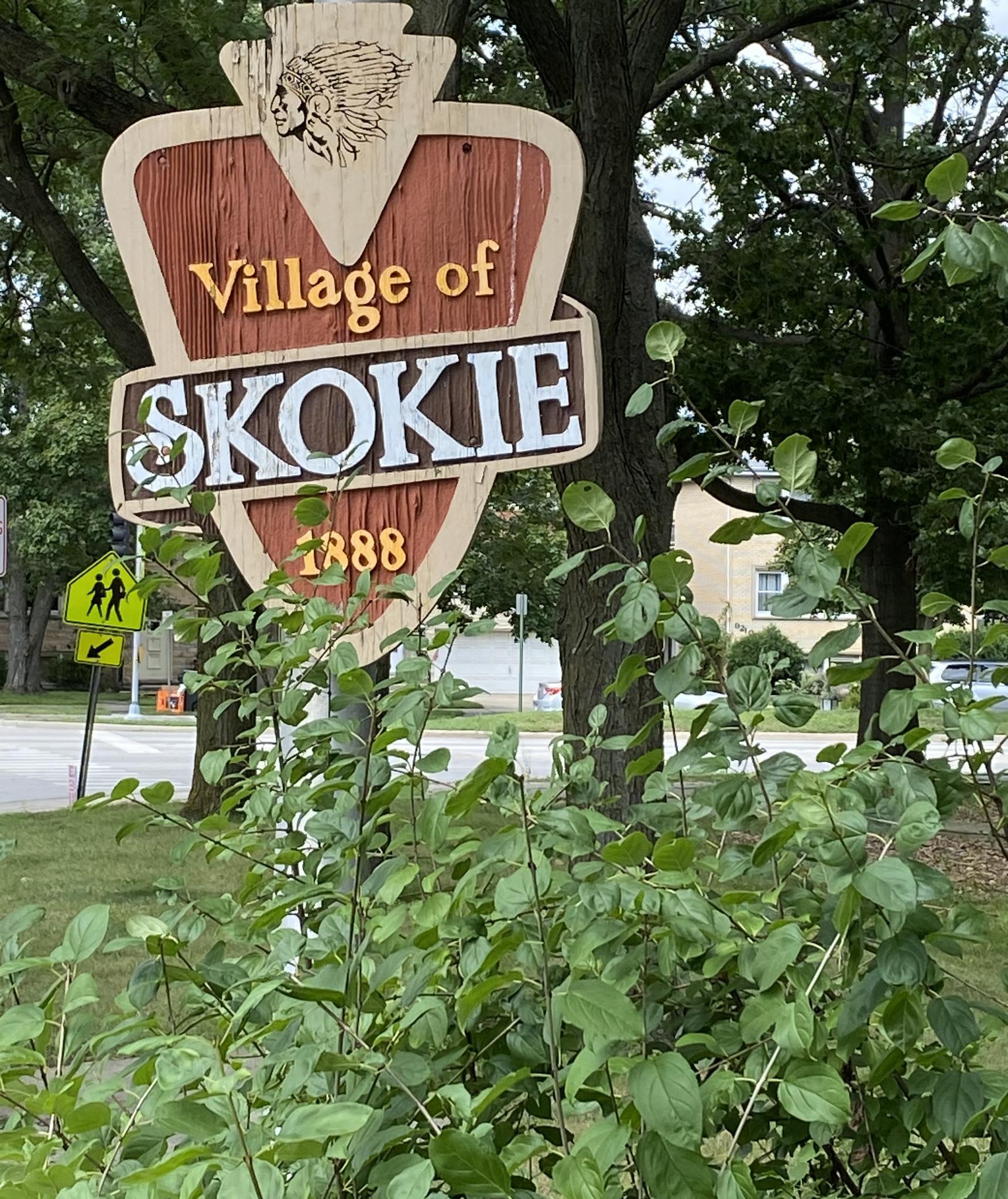 A wooden sign with text, surrounded by green leaves and tree branches.