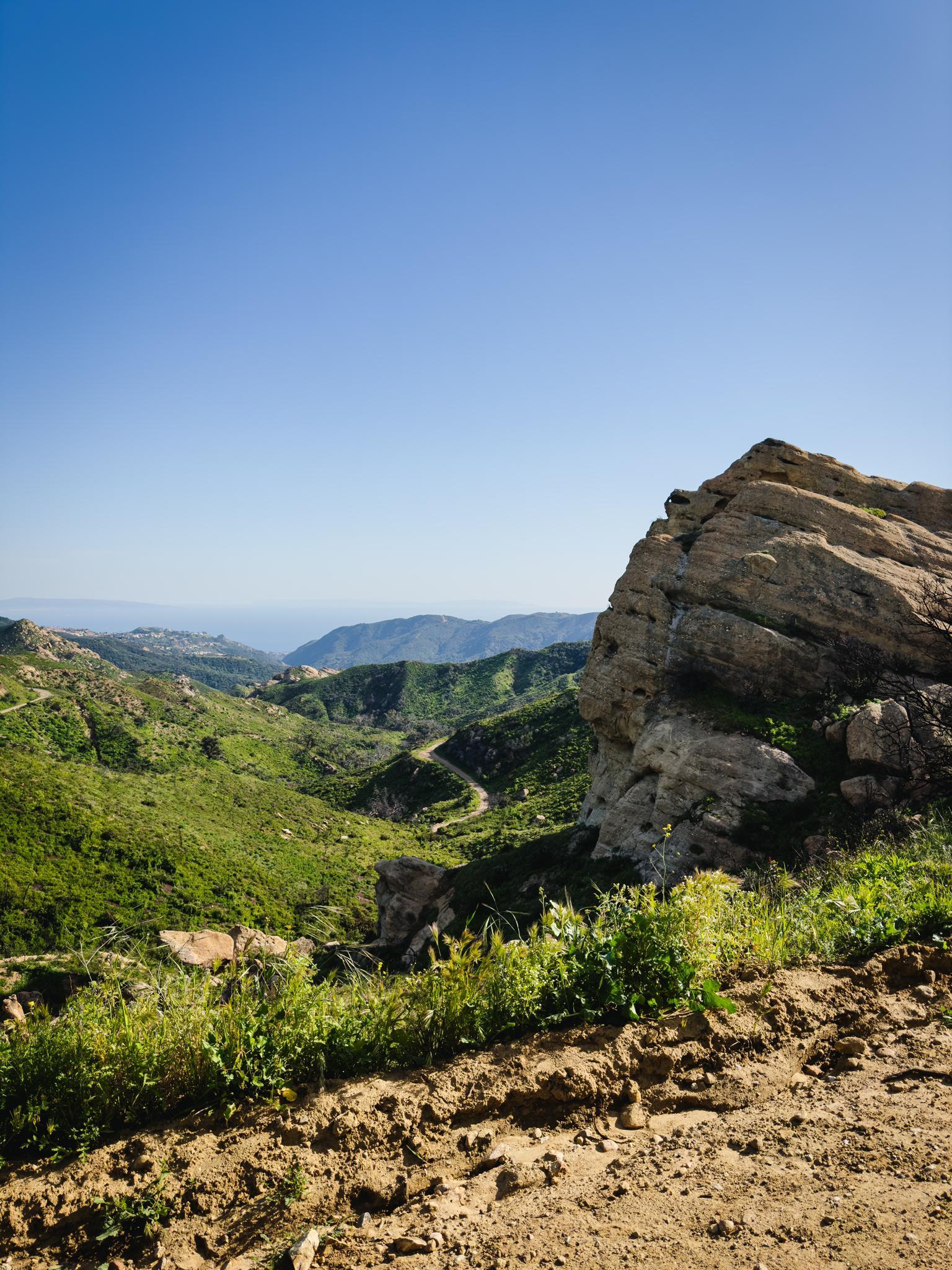 Large rock formation overlooking a green valley and distant ocean on a sunny day.