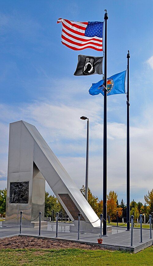 Modern monument and three flags flying under a clear blue sky. - Freeman Loop