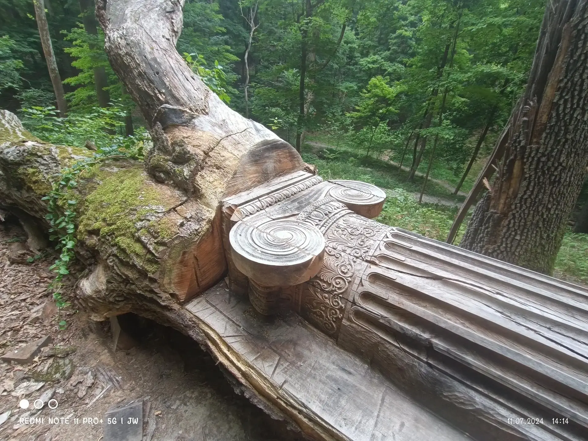 Intricately carved wooden bench resembling a column in a green forest.