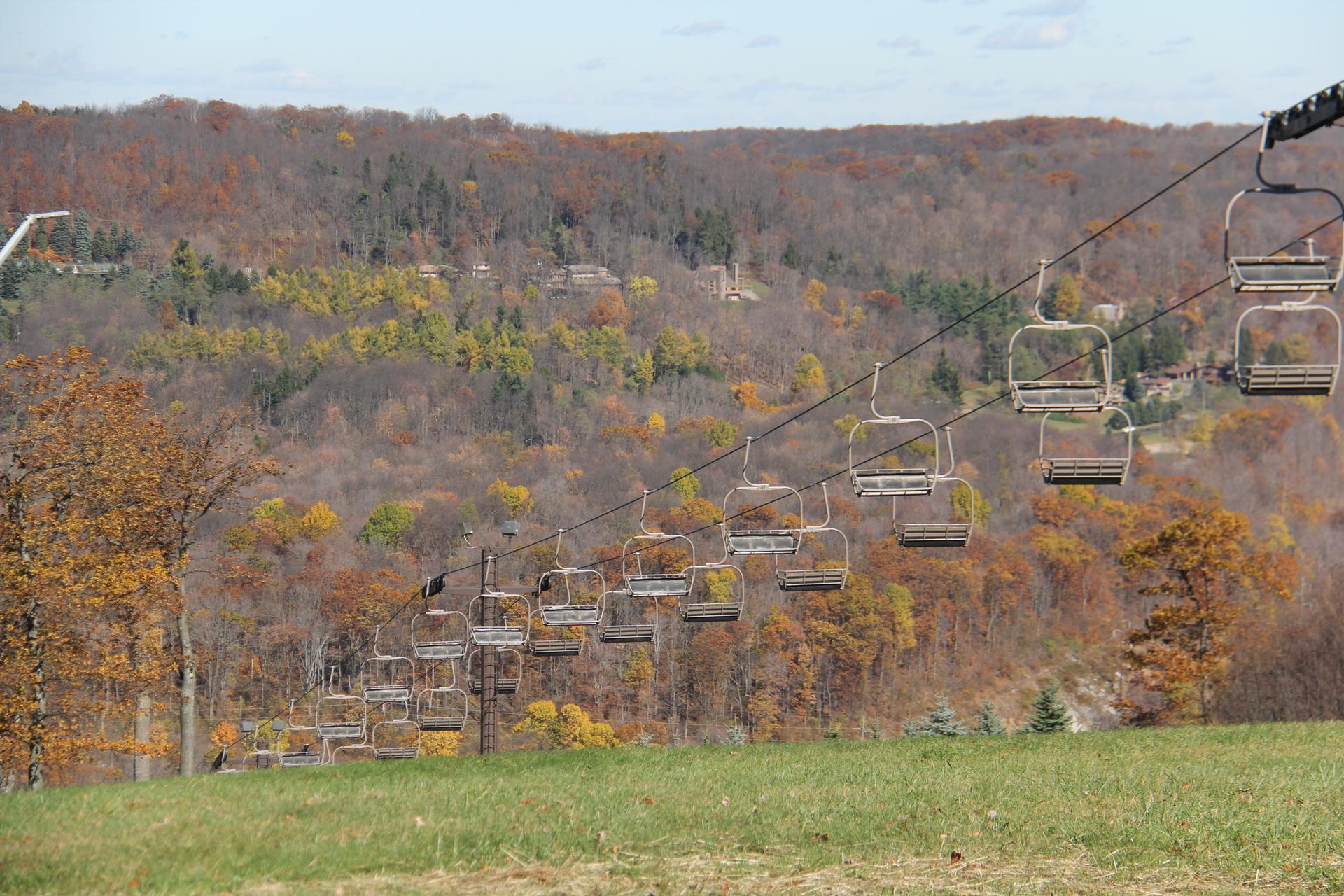 Empty ski lift chairs ascend over autumn hills on a bright day.