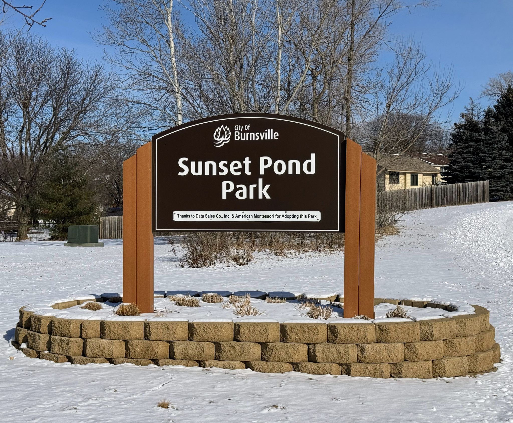 Park sign on a stone base in a snowy landscape with bare trees. - Sunset Pond